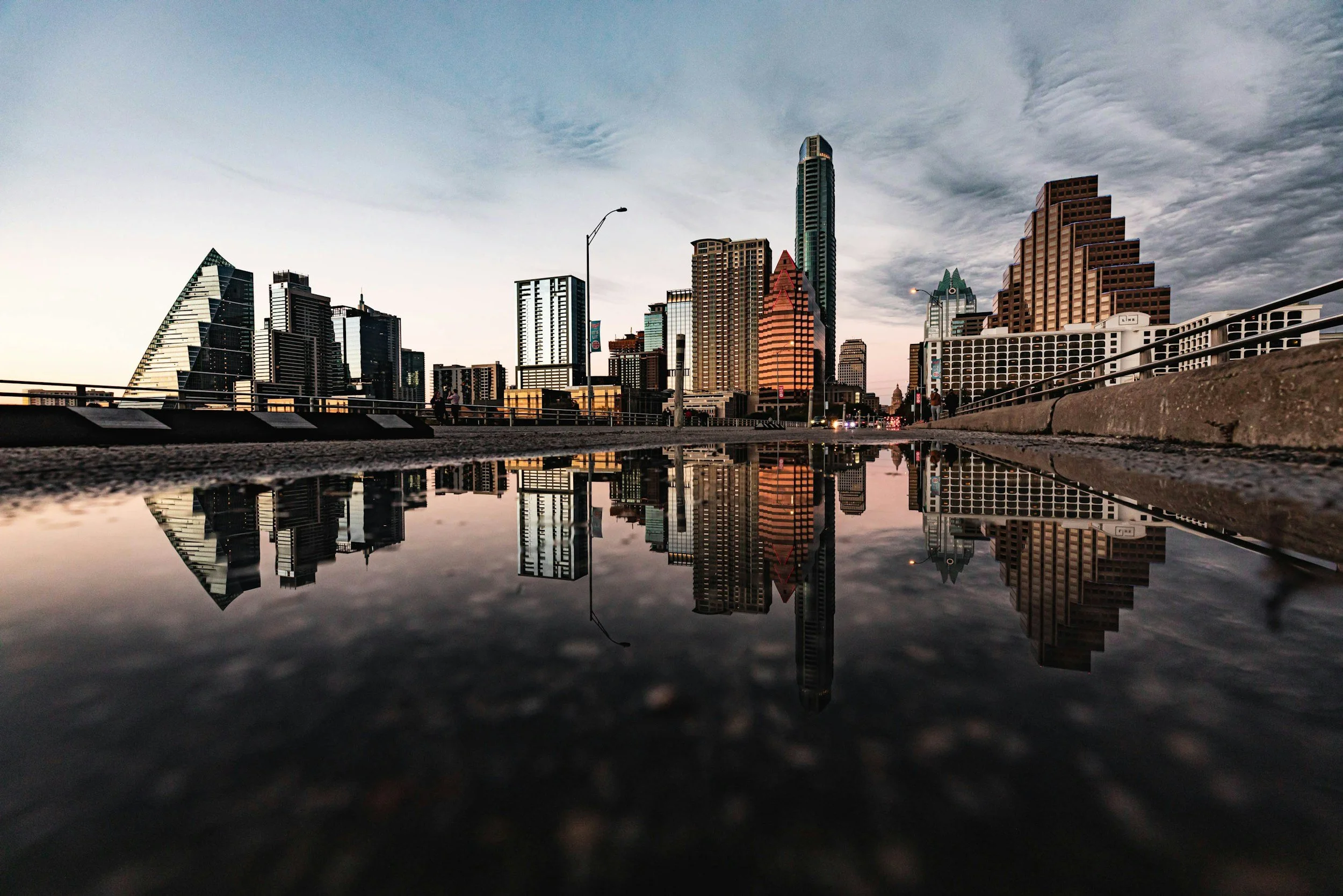 City skyline with tall skyscrapers reflected in a puddle on the ground.