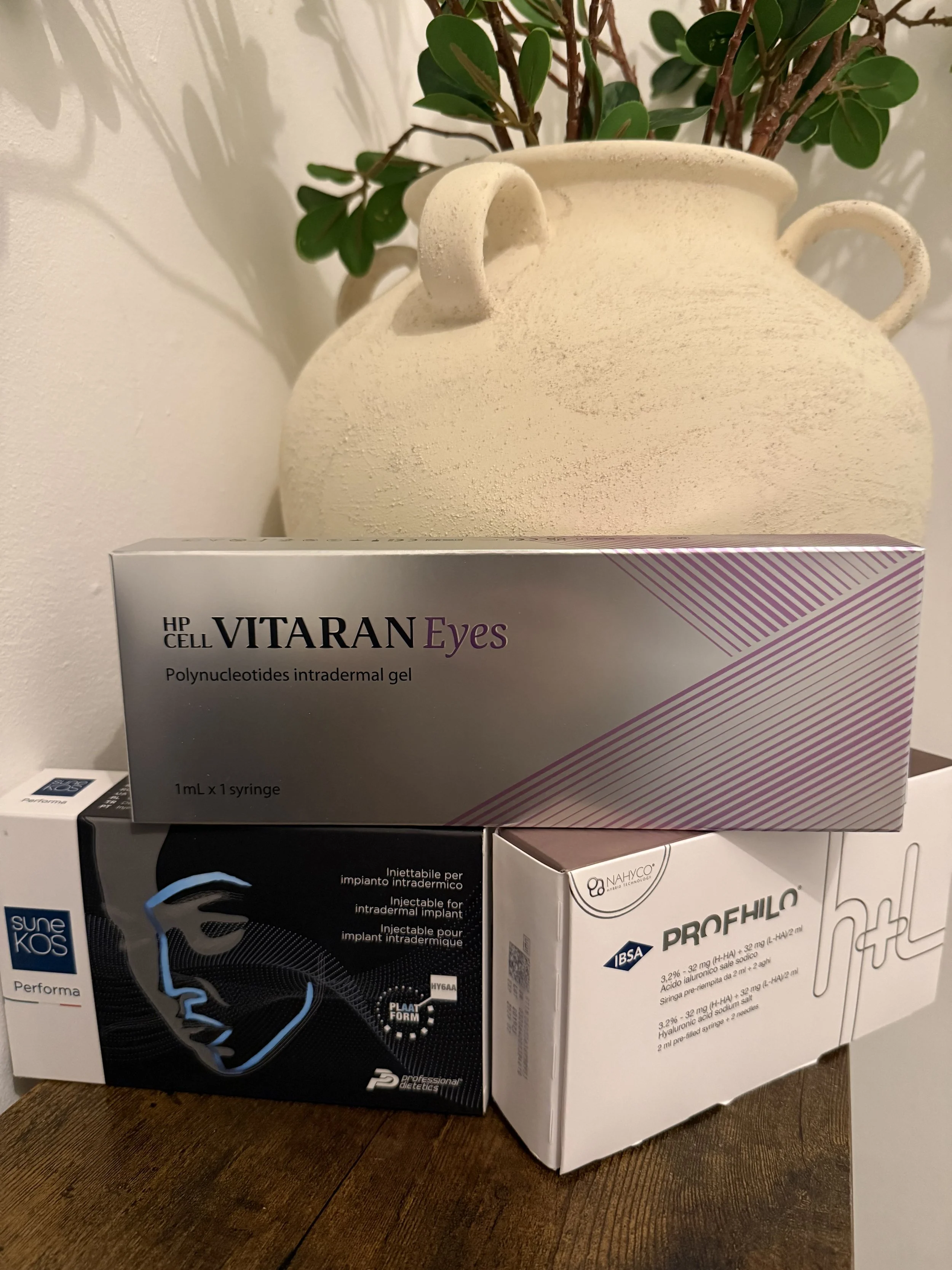 A person receiving a cosmetic facial treatment with a gold-colored device emitting blue light, with a skincare product labeled 'Bontia Mora' held above the person's face.