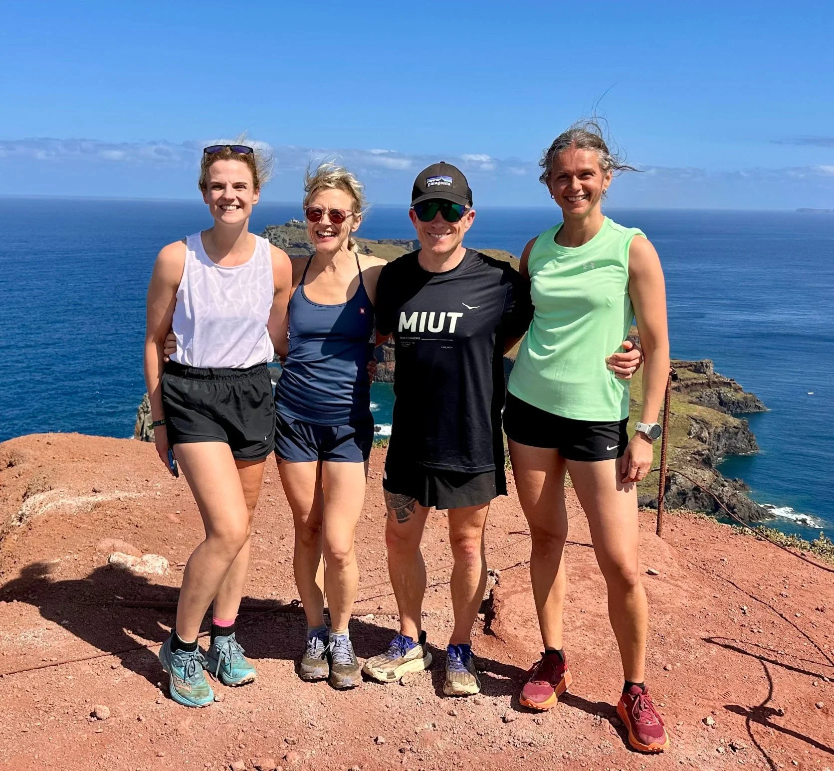 Four people posing on a rocky cliff overlooking the ocean on a sunny day.