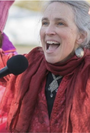 A photo of a white woman in red singing into a microphone.