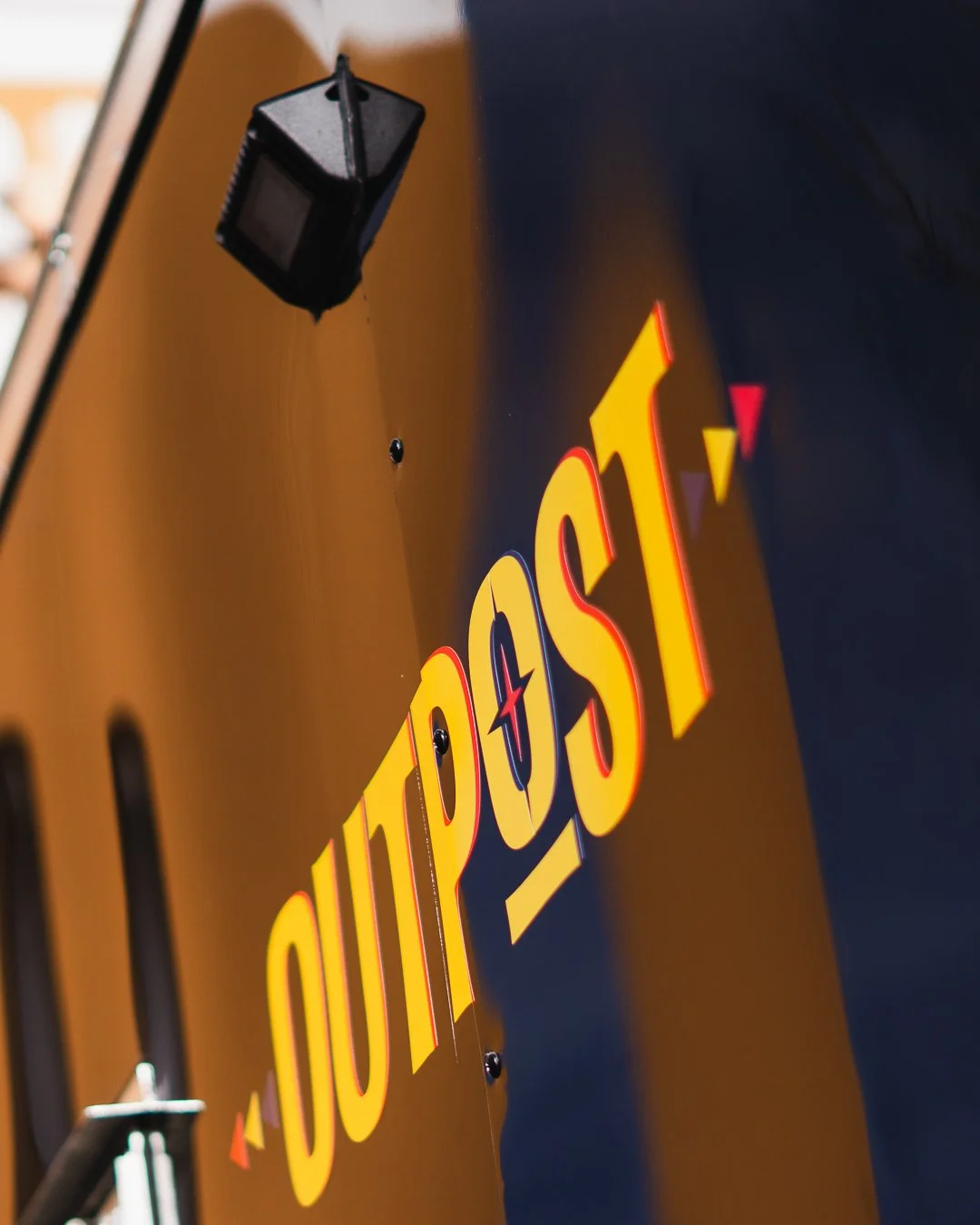 Close-up of a yellow and red 'OUTPOST' logo on a black food truck.