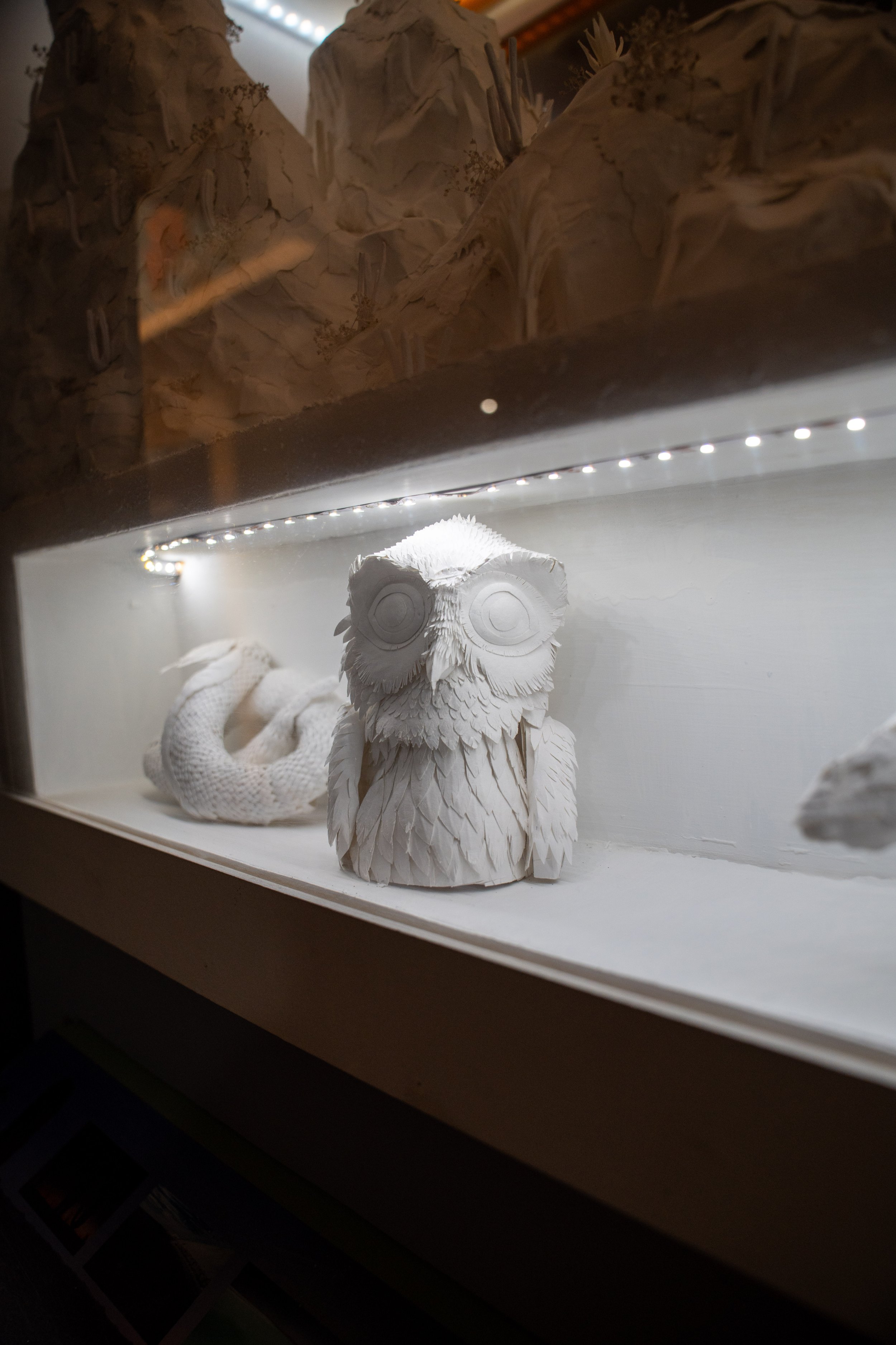 Una figura de búho de color blanco, con plumas detalladas, exhibida en un estante con iluminación.