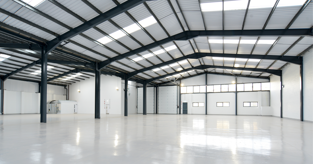 Empty industrial warehouse with high ceiling, metal beams, and large garage doors.