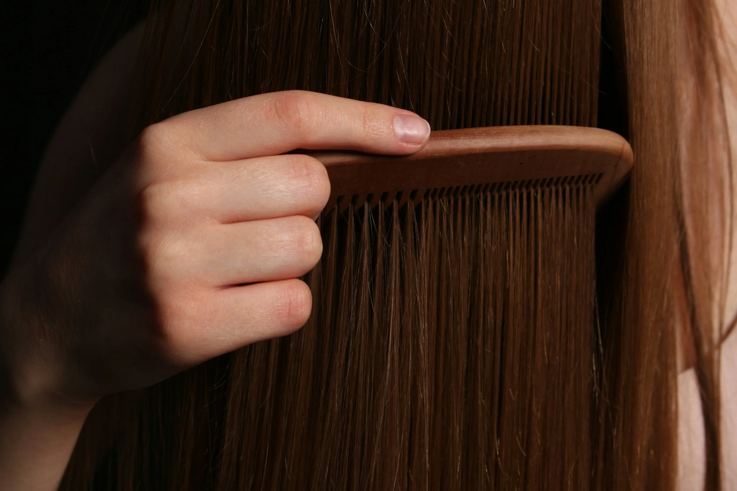 A person brushing long, straight brown hair with a wooden comb.