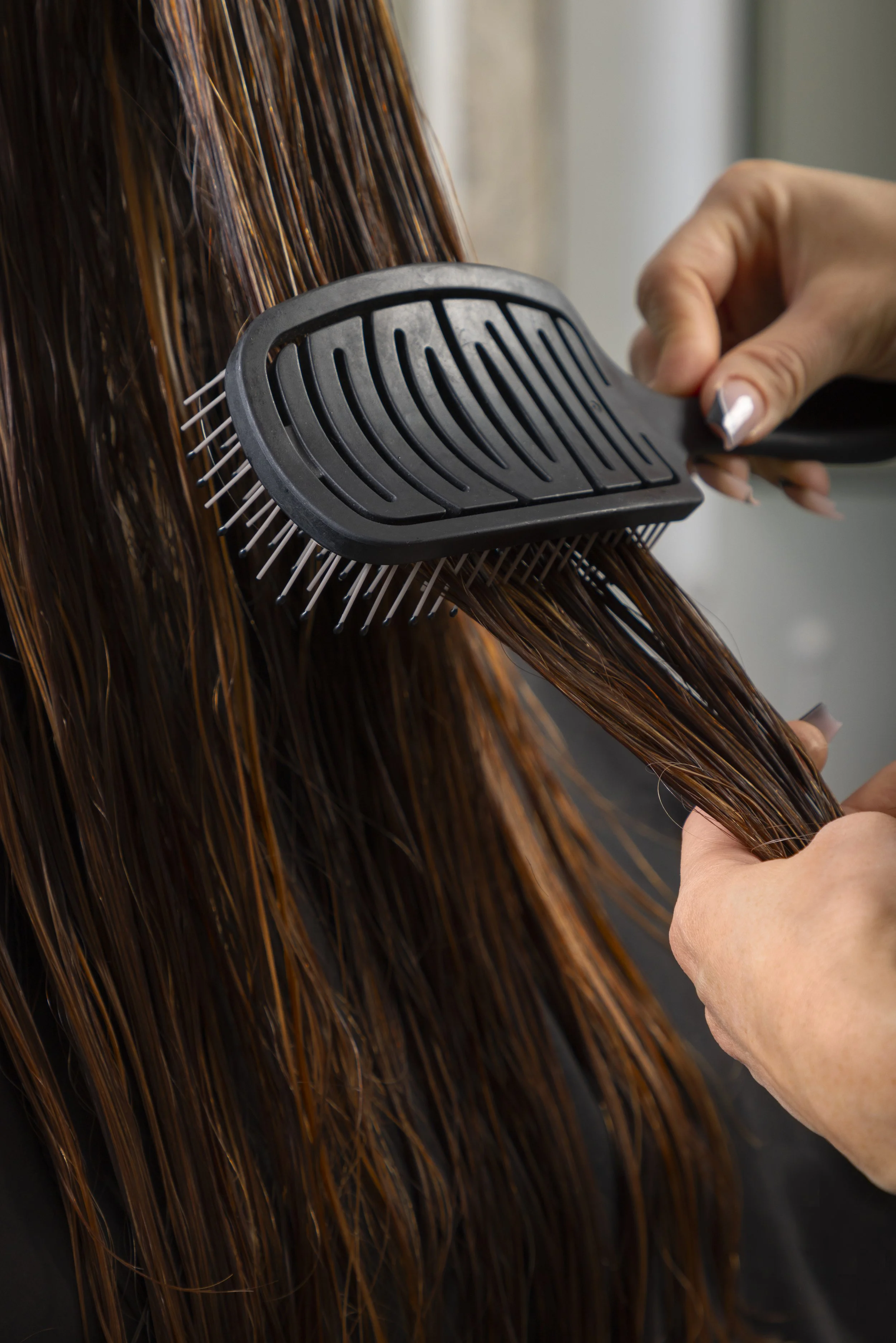 Person brushing wet, brown hair with a wide-tooth comb.
