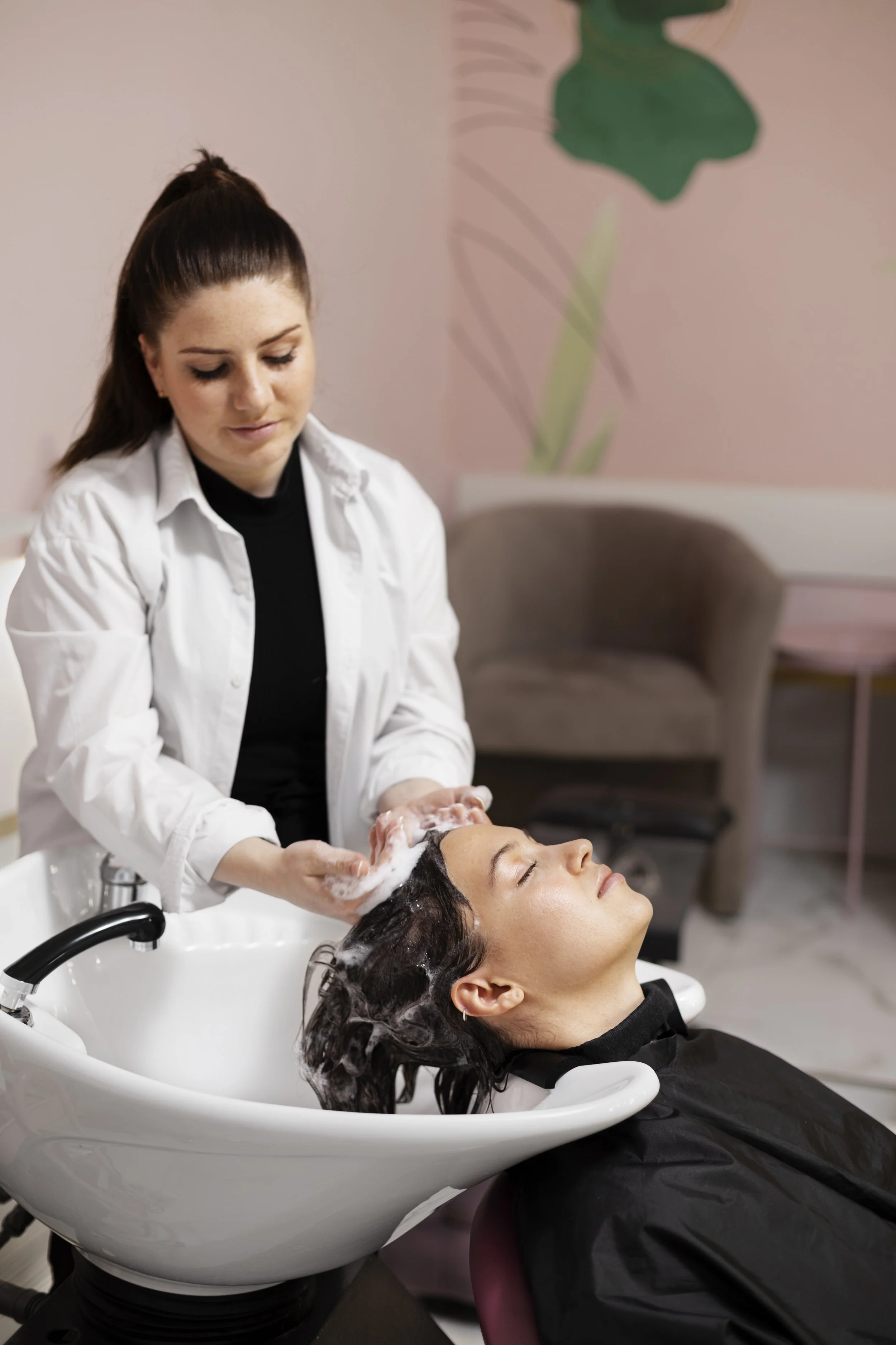 A woman getting her hair washed at a salon while lying back with her eyes closed as a stylist shampoos her hair.