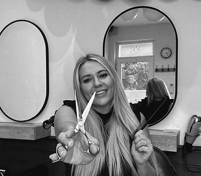 Young woman smiling and holding scissors and a hand mirror inside a salon