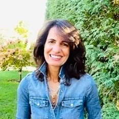 Ana Jardim Messenger smiling and wearing a denim jacket, with trees and greenery in the background.
