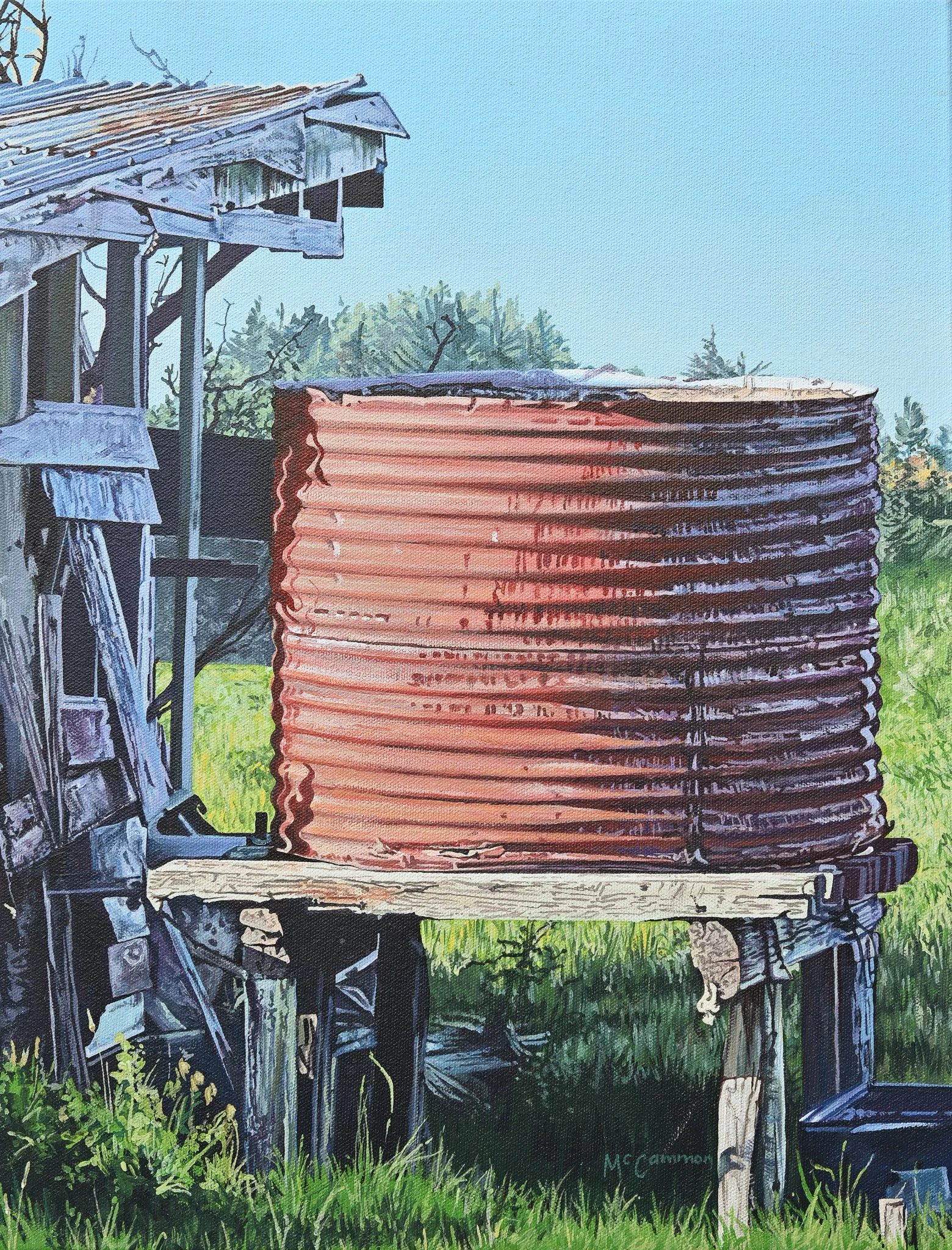 A weathered wooden structure with a large rusted corrugated metal water tank on a platform, surrounded by green grass and trees, and a clear blue sky in the background.