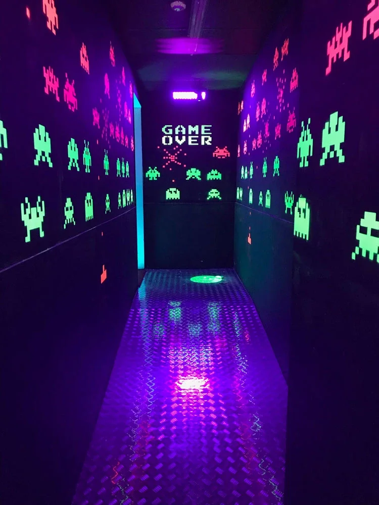 A neon-lit hallway decorated with pixelated alien and spaceship figures, reminiscent of retro video games, with a large 'GAME OVER' message at the end.