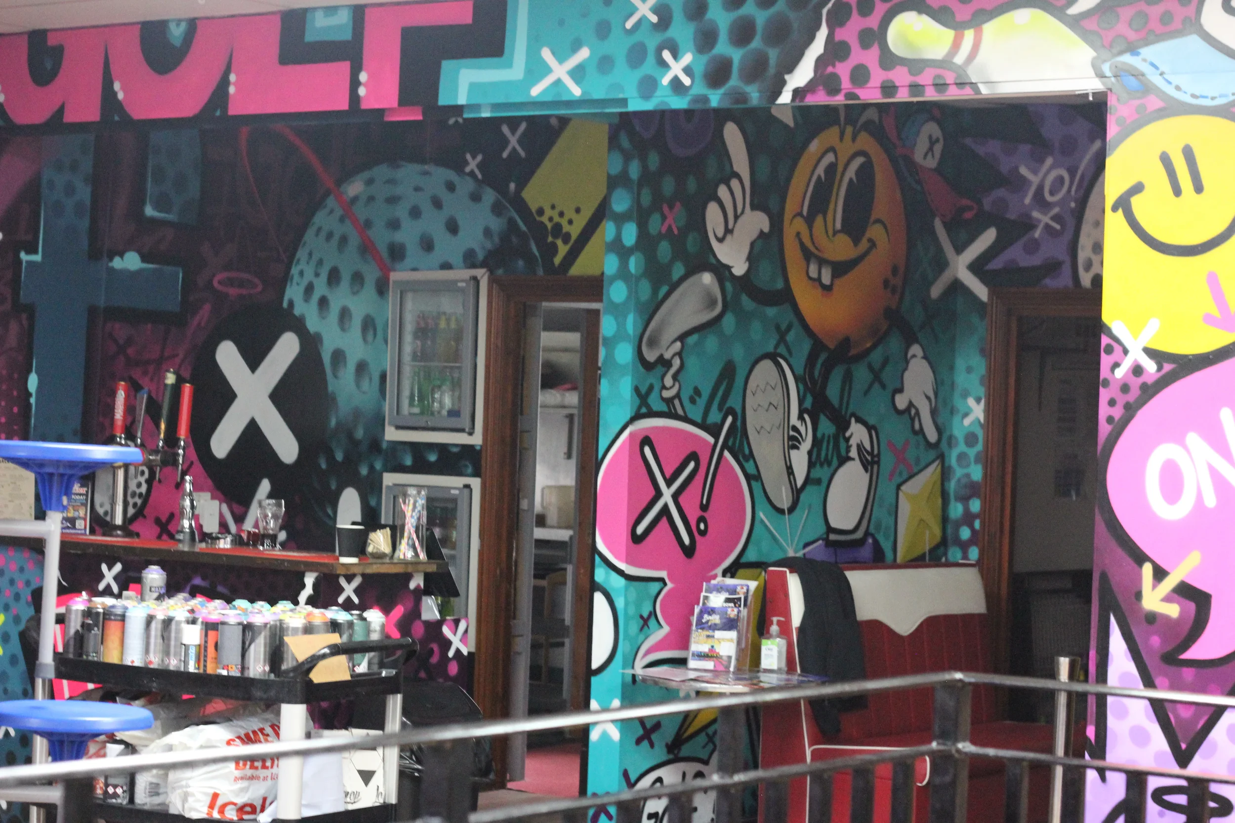 Colorful graffiti wall with cartoon-style characters and speech bubbles, featuring a smiling face with a tongue sticking out and speak bubbles with Xs and slashes.