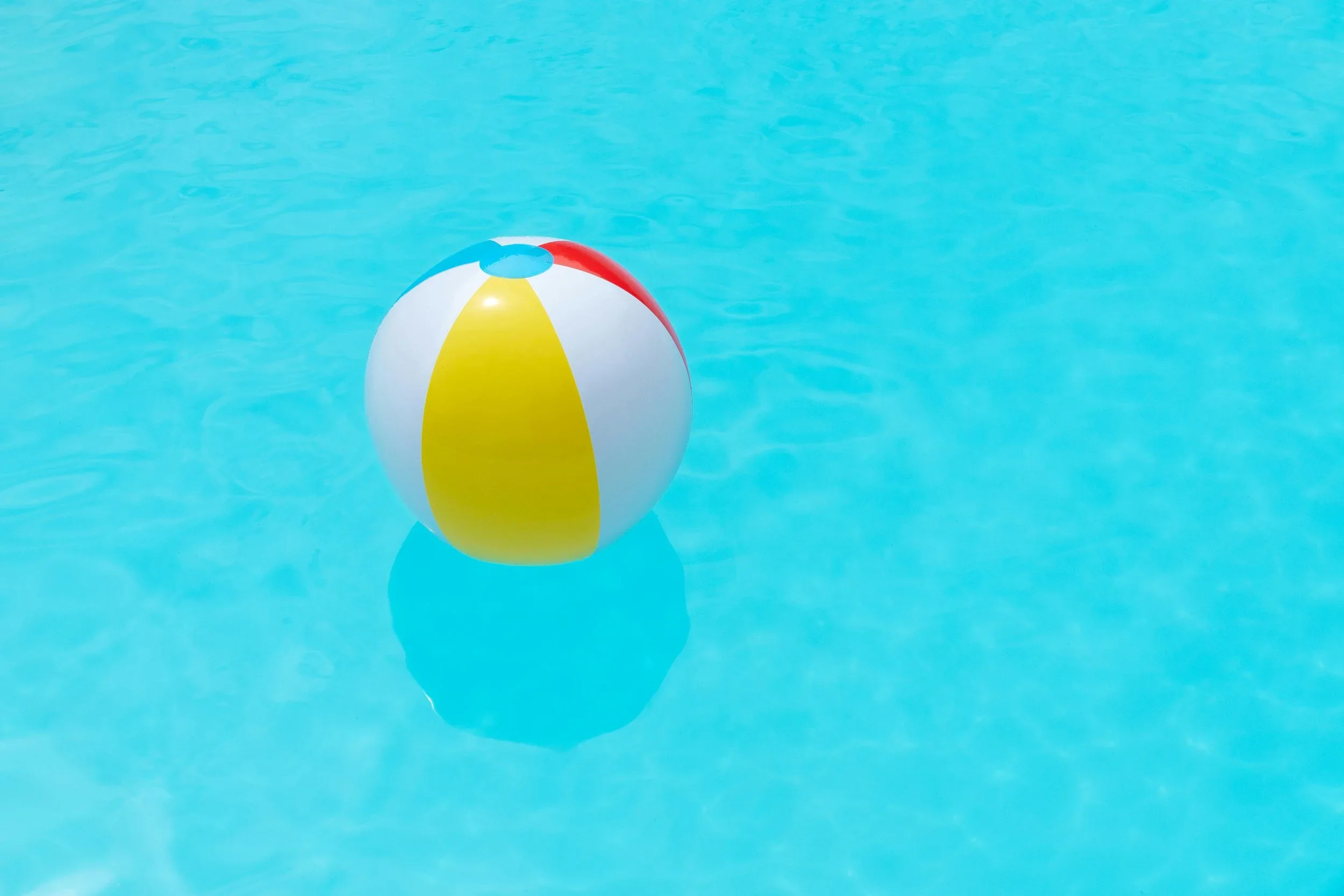Colorful beach ball floating in a clear blue swimming pool.