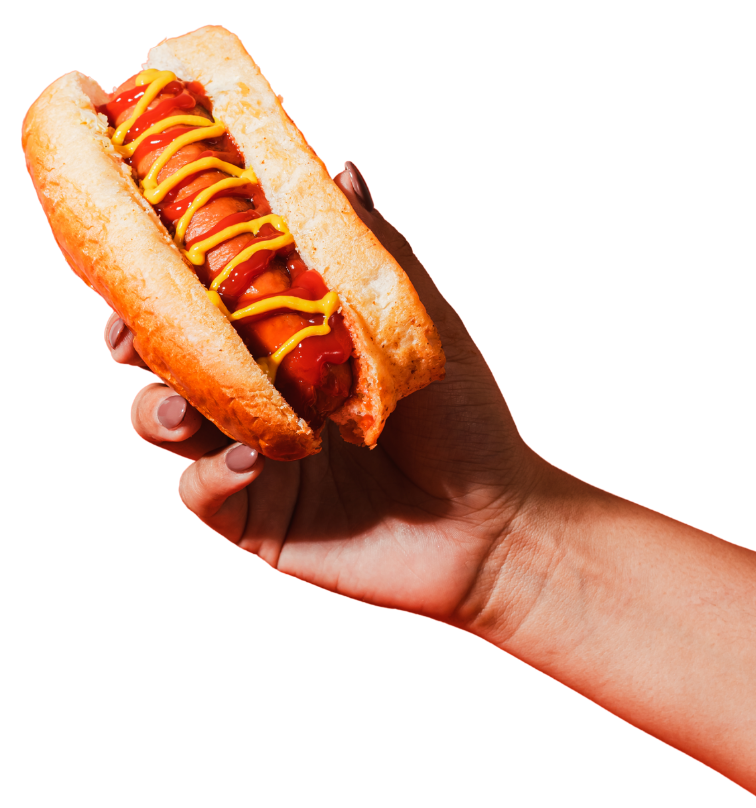 Close-up of a person's hand holding a hot dog in a bun with ketchup, mustard, and relish.