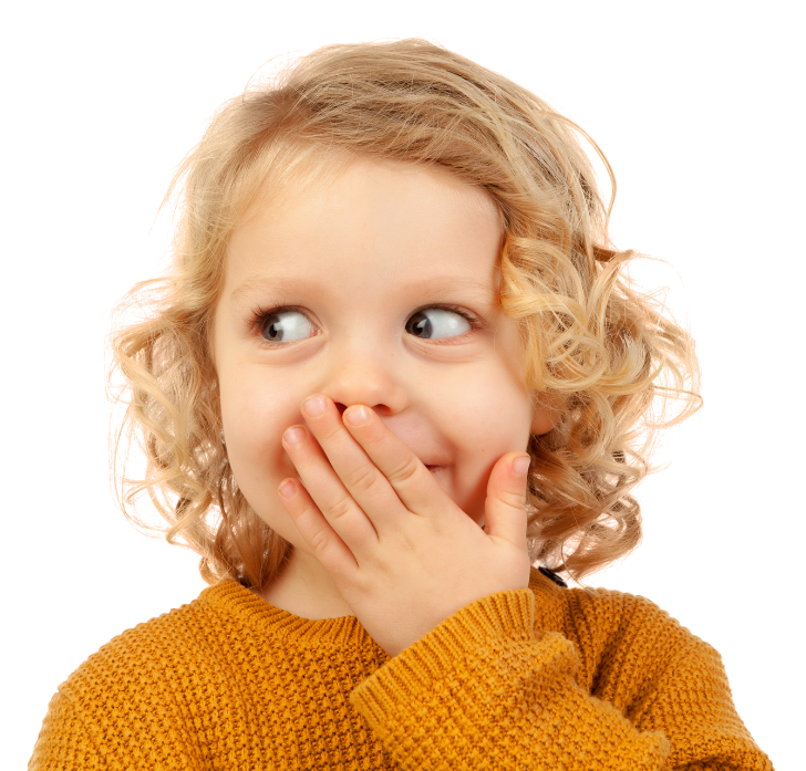 A young girl with curly blonde hair wearing a mustard yellow sweater covers her mouth with her hand while glancing sideways.