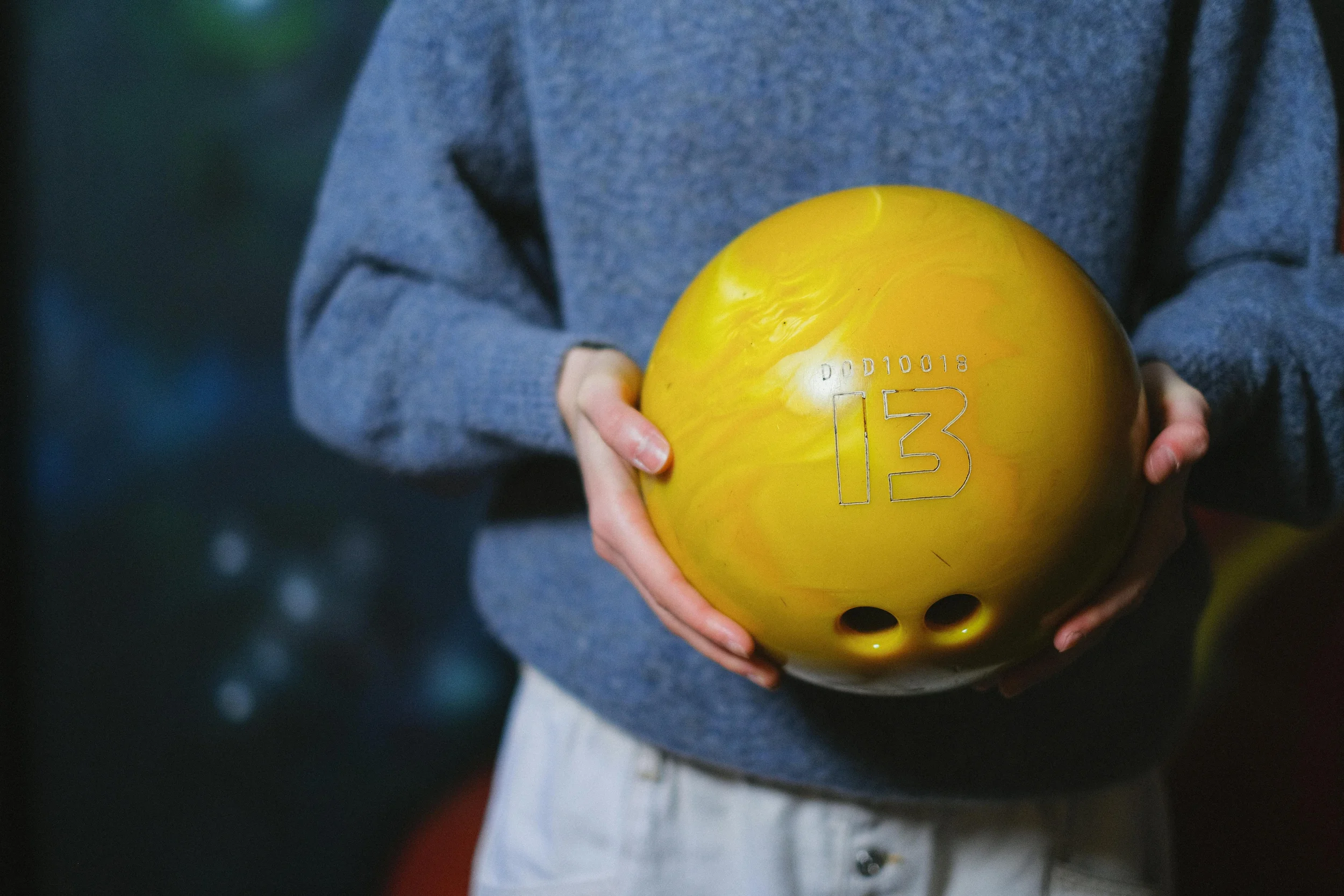 Person holding a yellow bowling ball with the number 13 and some numbers engraved on its surface.
