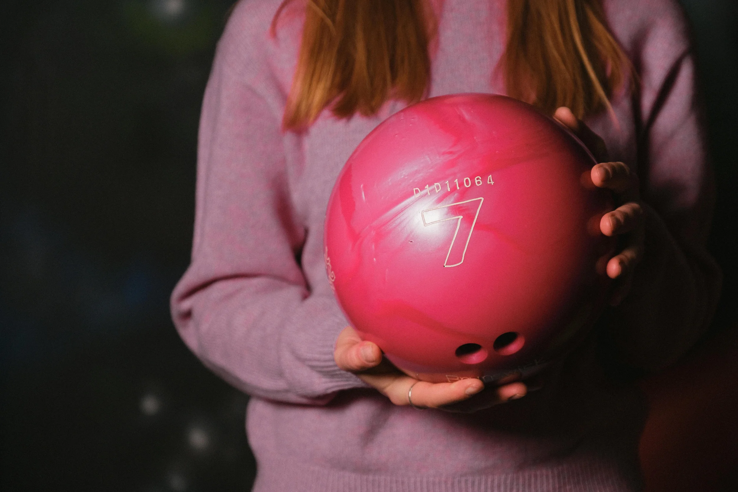 Person holding a pink bowling ball with the number 7 on it.