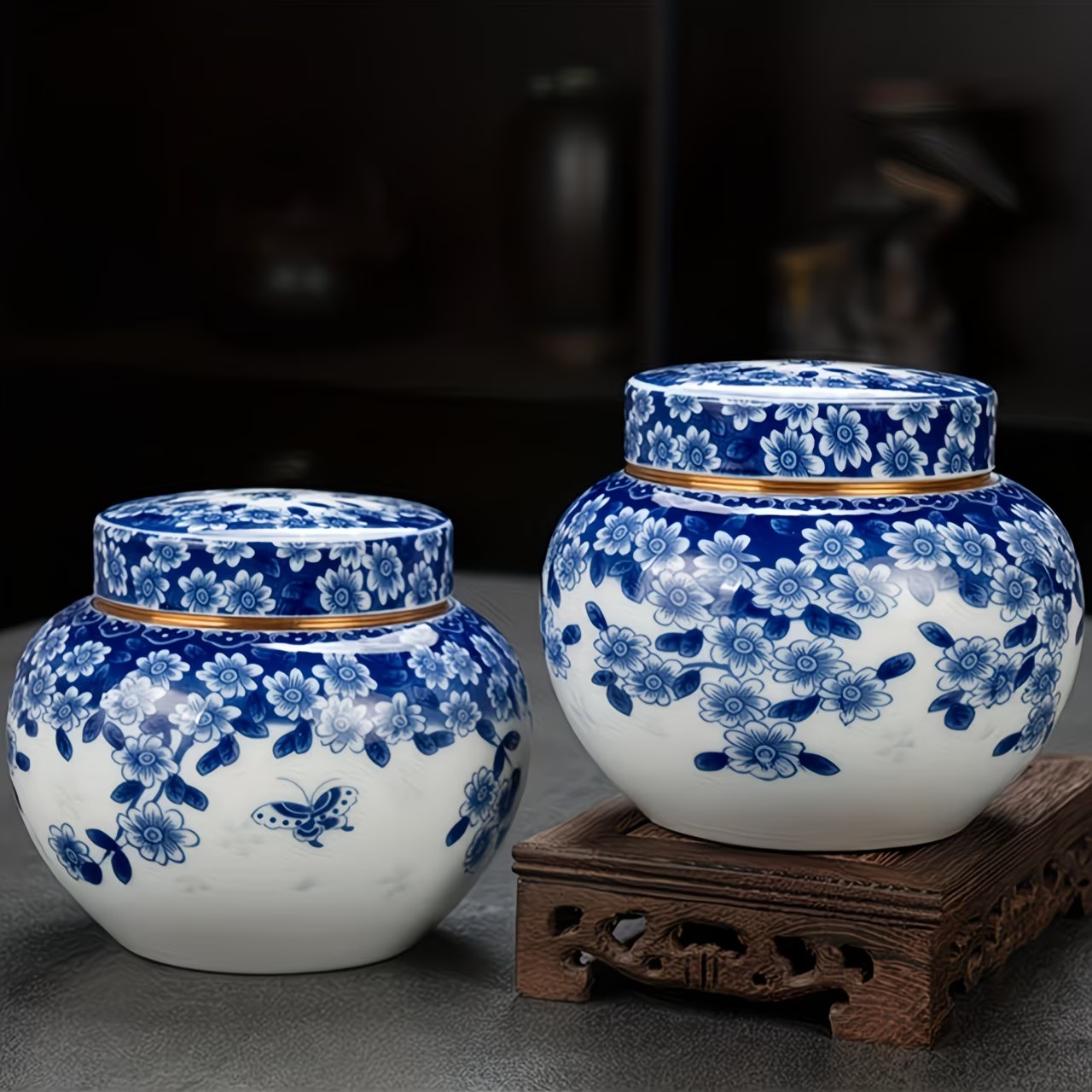 Two white ceramic jars with blue floral patterns and gold trim on a wooden stand