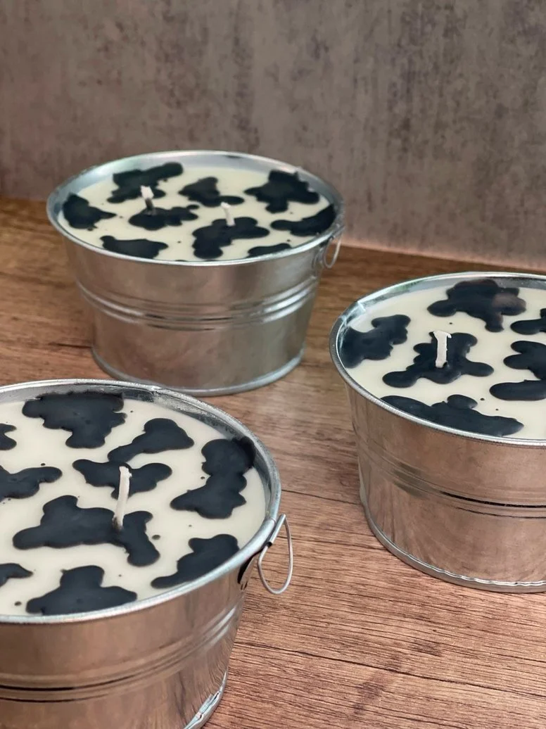 Three white candles with black dog silhouette patterns in small metal buckets on a wooden surface.