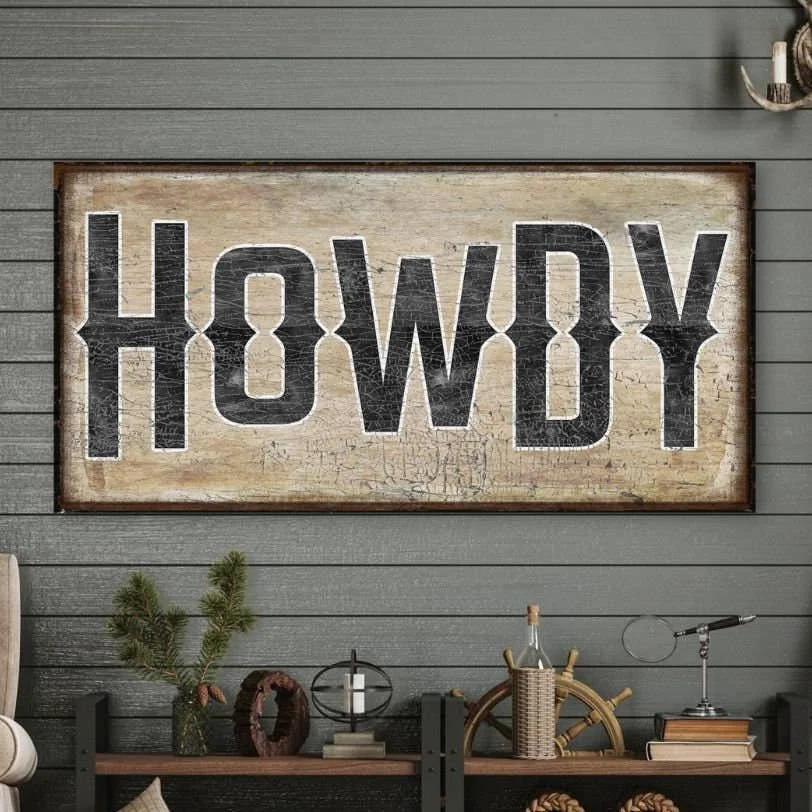 A rustic sign with the word "HOWDY" printed in black, placed on a gray wooden wall.