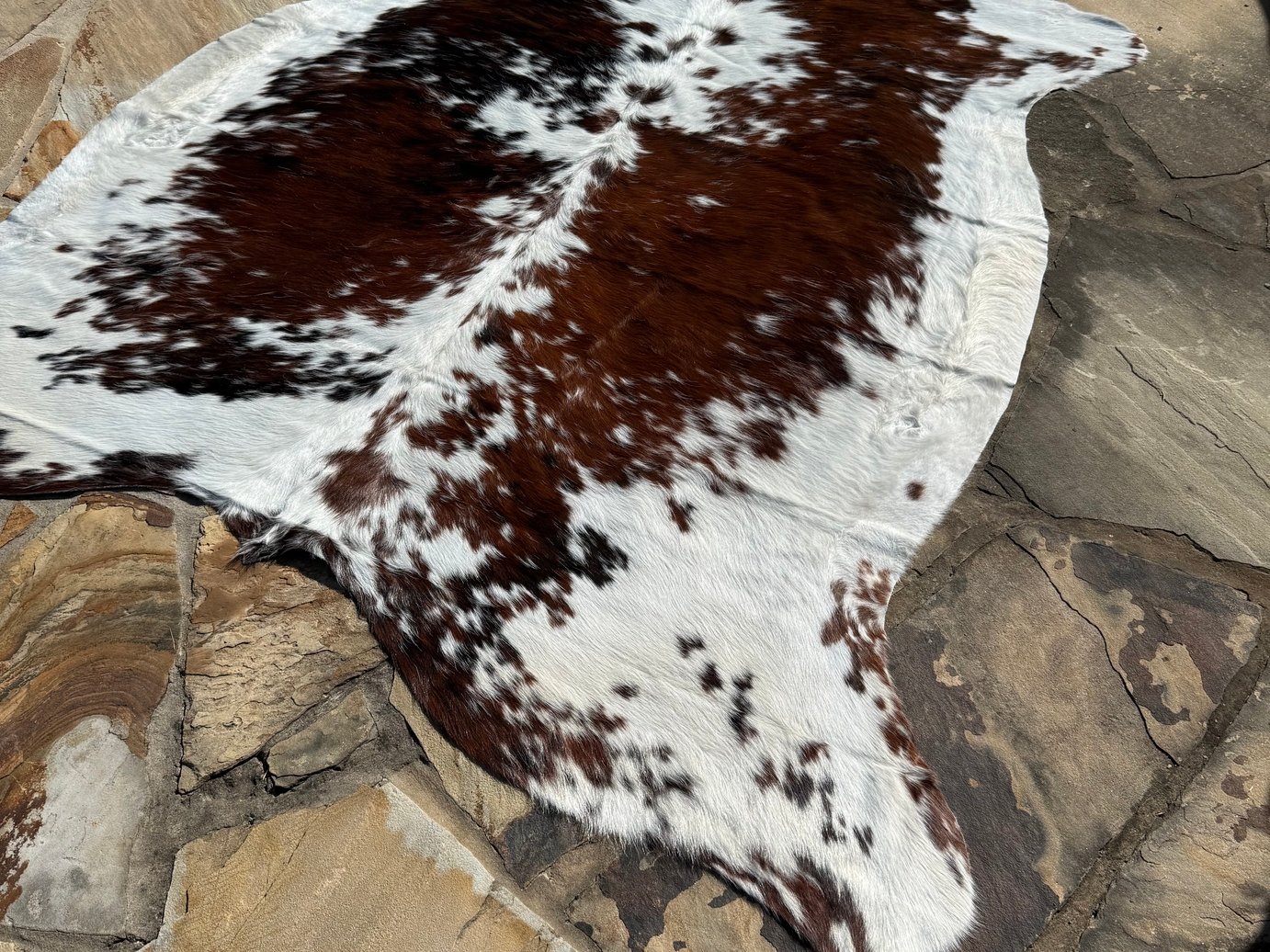 A cowhide rug with white, brown, and black spots, laid on a stone floor.
