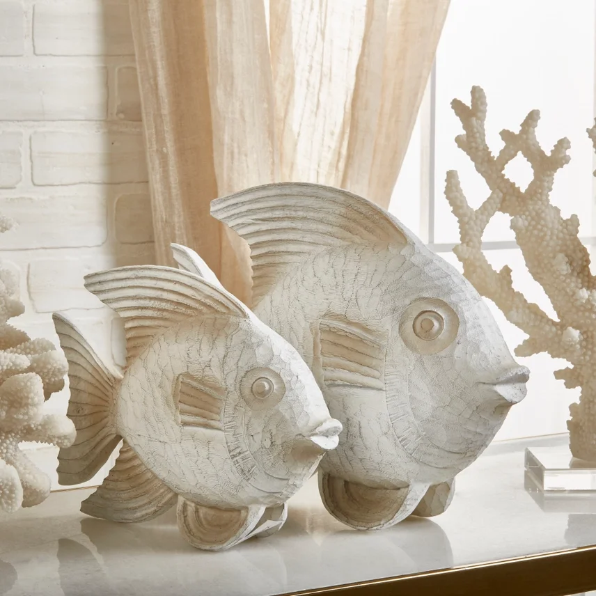 Decorative fish sculptures made of white shell material, placed on a surface with coral sculptures in the background.
