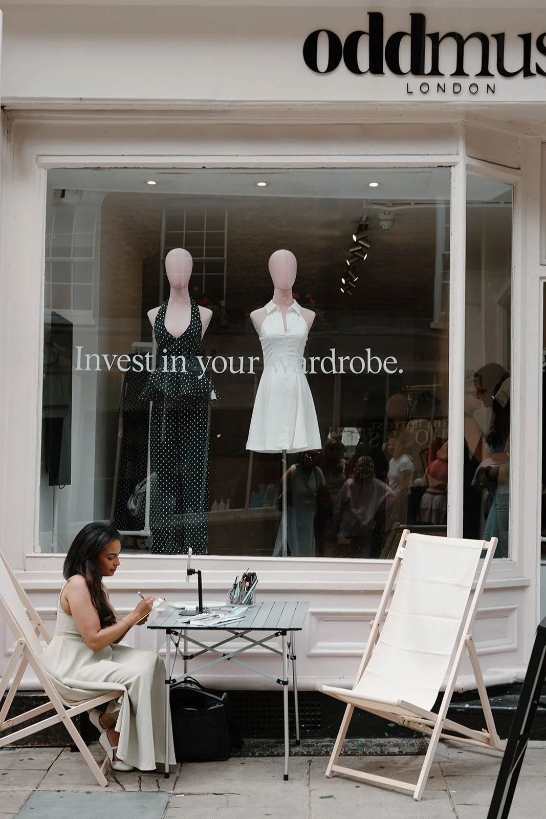 A woman sitting outside Odd Muse clothing store Covent garden, drawing and painting customers
