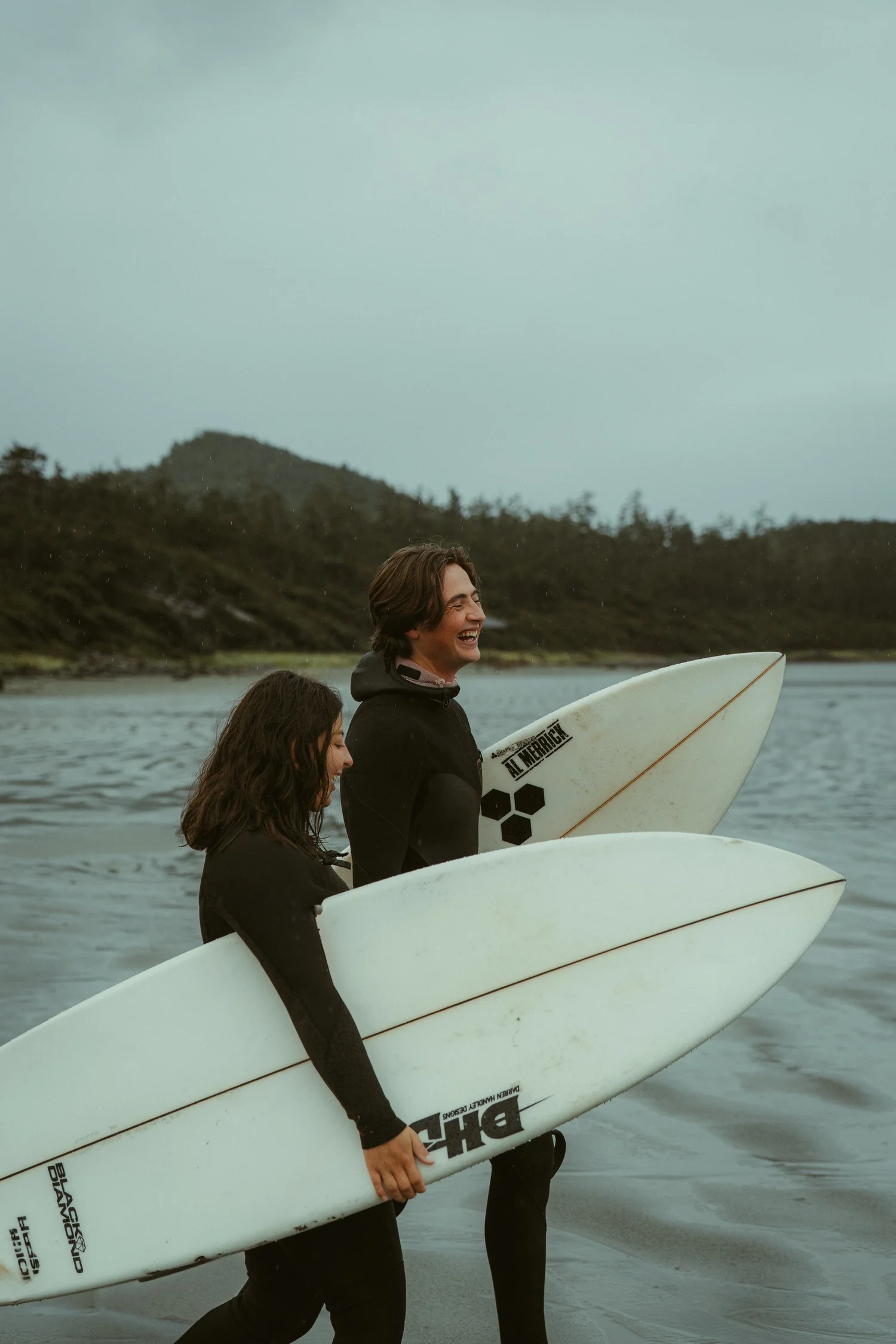 Couple laughing together while carrying surfboards from the water