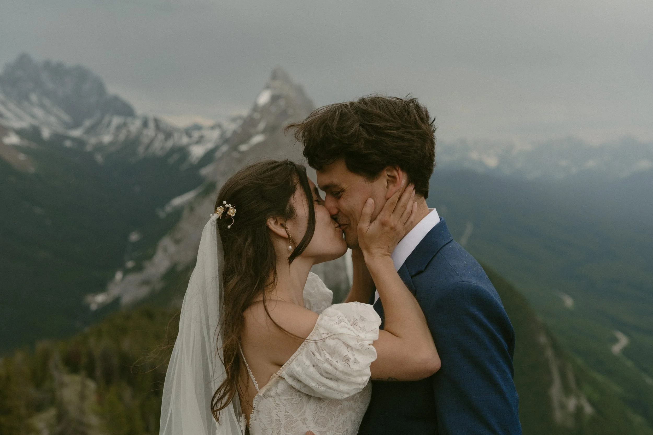 Couple in wedding attire kissing with mountains in the background