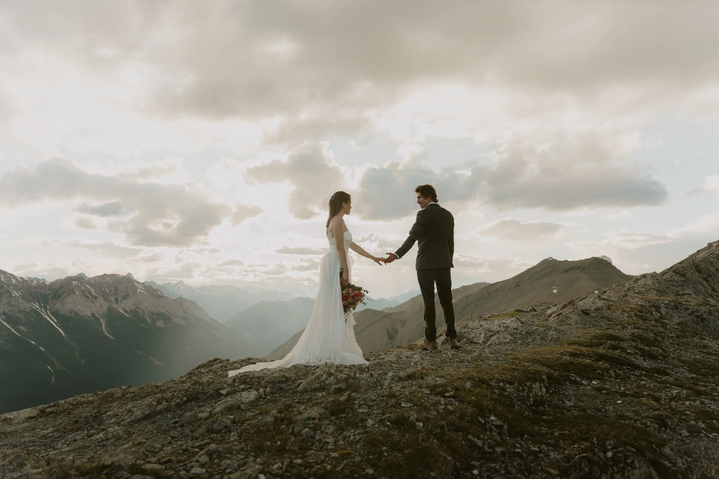 Couple in wedding attire on the Ha Ling Peak summit at sunset above Canmore