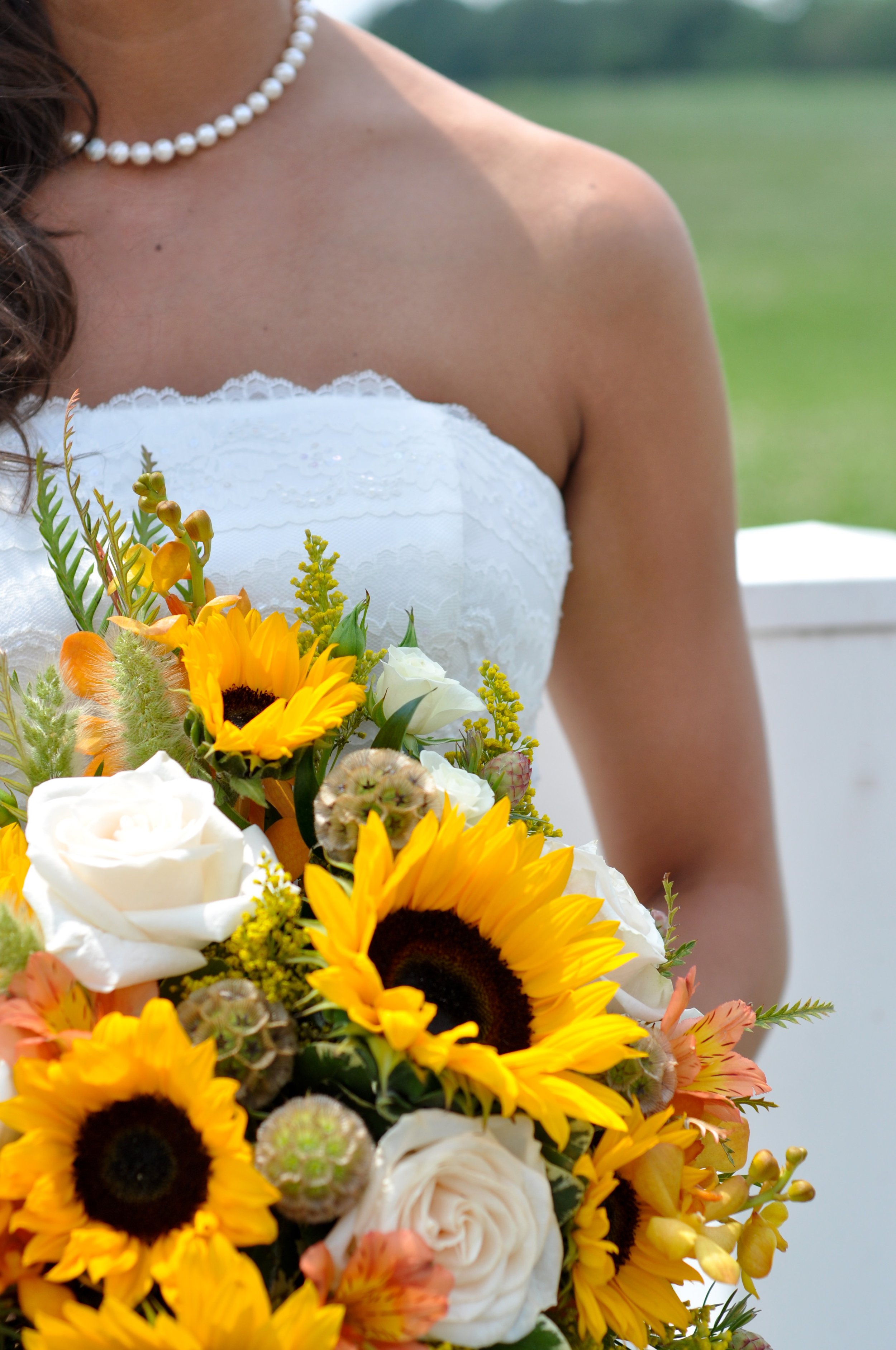 A bride in a white strapless wedding dress holding a bouquet of sunflowers, white roses, and other flowers.