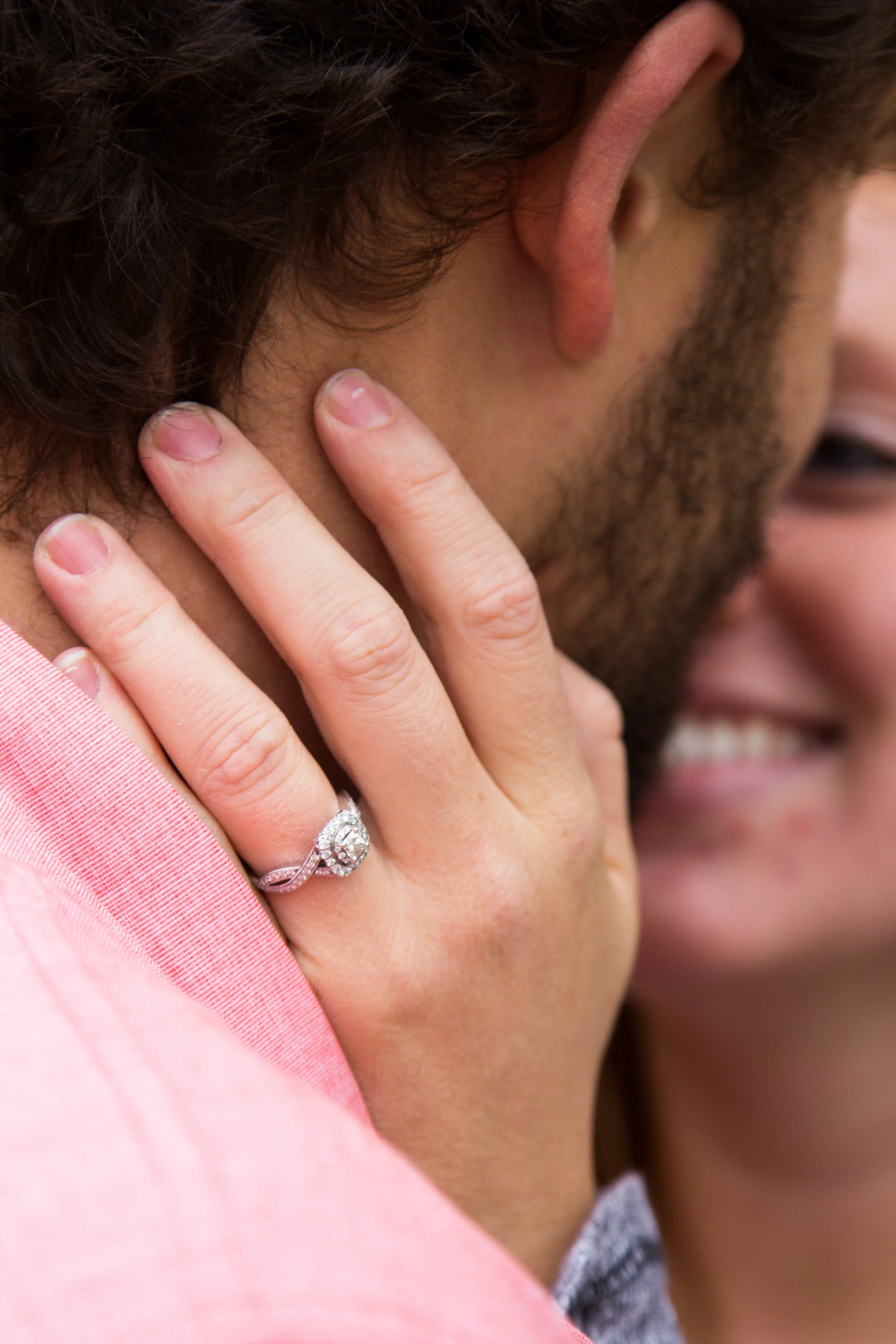 Close-up of an engagement ring, touching a neck and smiling.