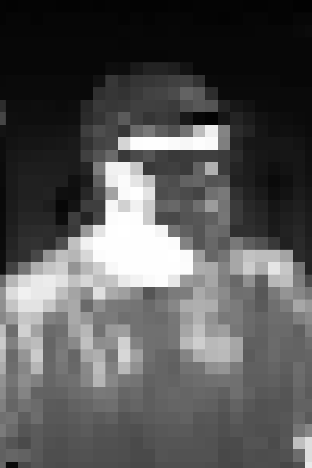 A person standing behind a table of food dishes at an event, wearing a checkered shirt and glasses.