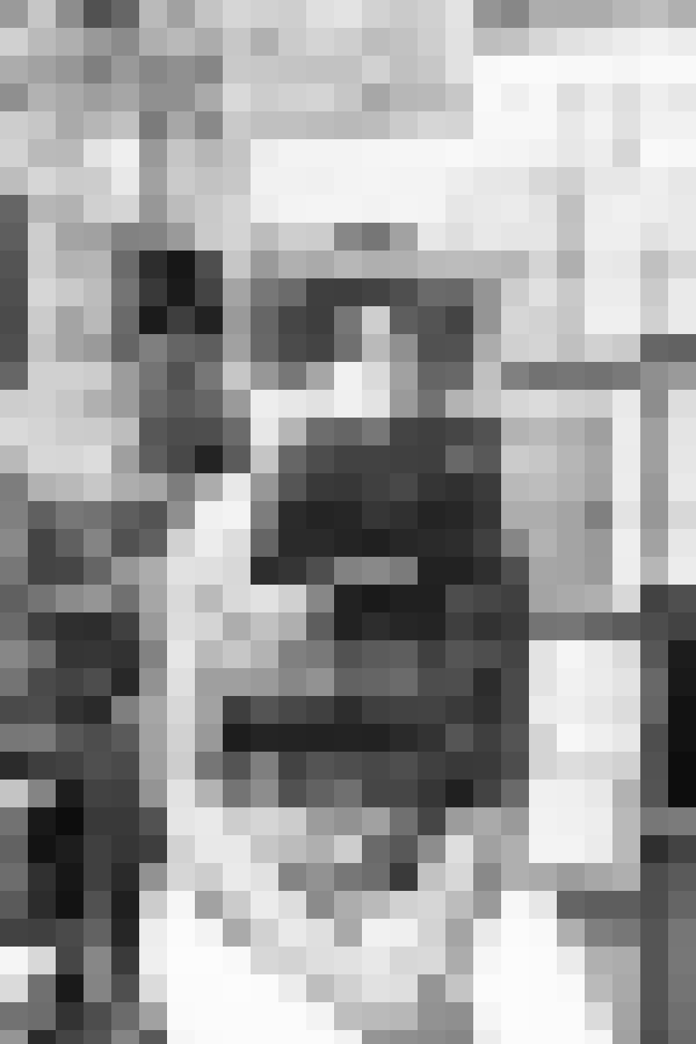 A person standing in a kitchen next to a stove and oven, preparing food, with kitchen cabinets and appliances in the background.