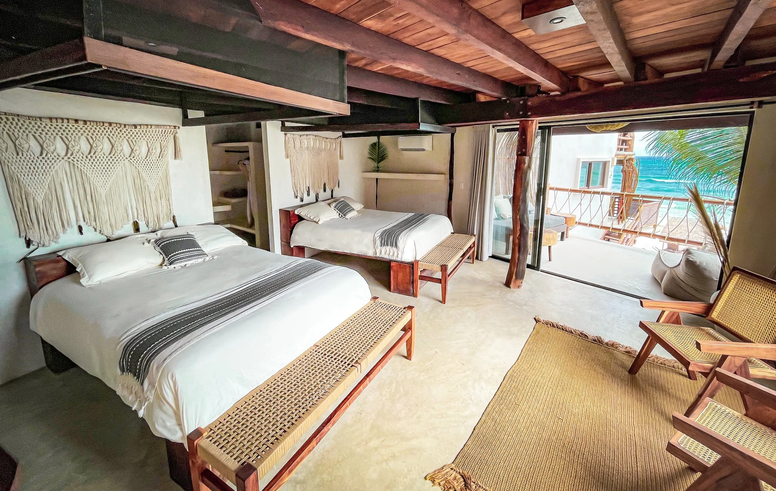 A hotel room with two beds, a balcony view of the ocean, and tropical decor.