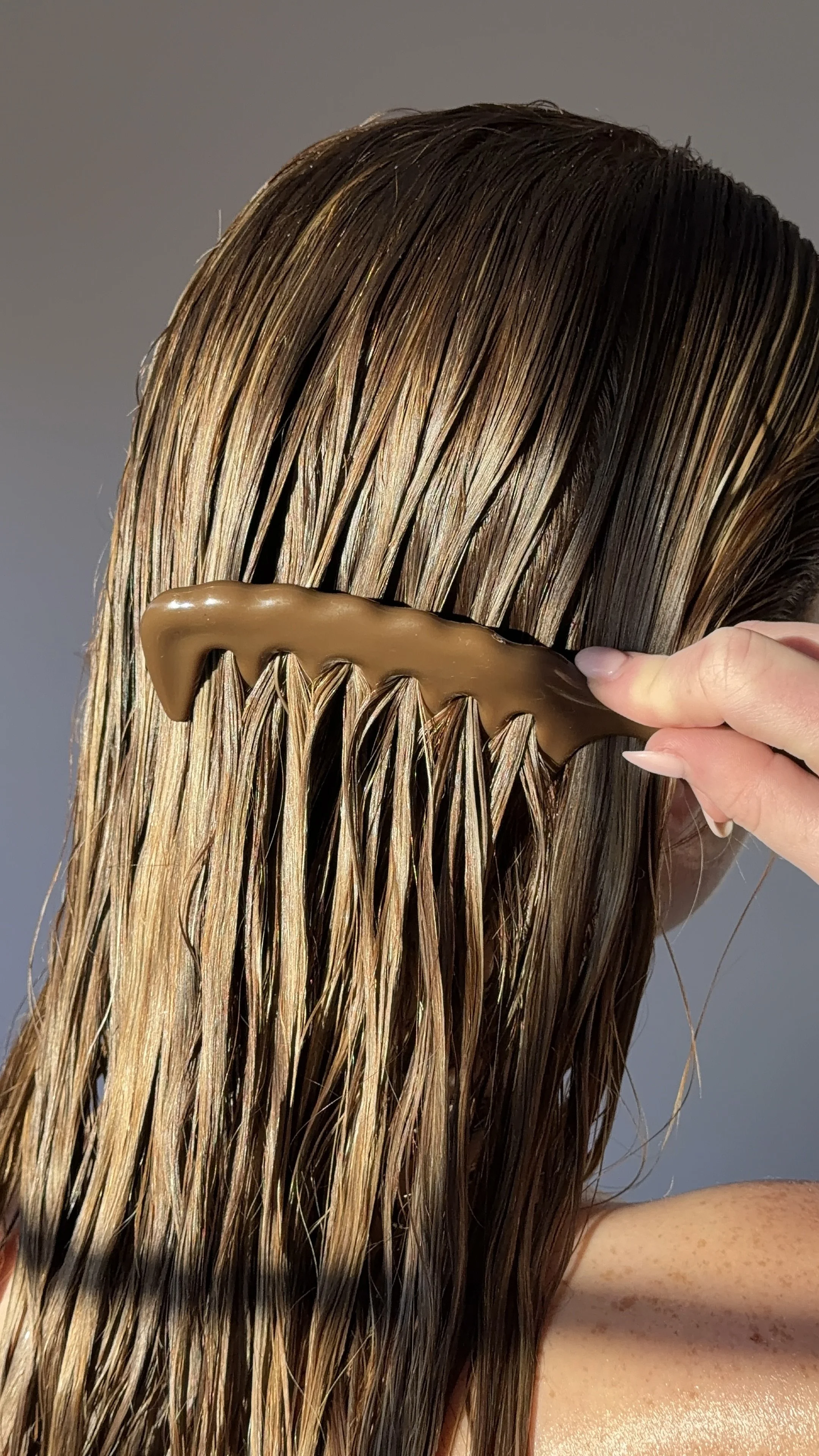Close-up of a person's hair being parted and detangled with a brown hair clip.