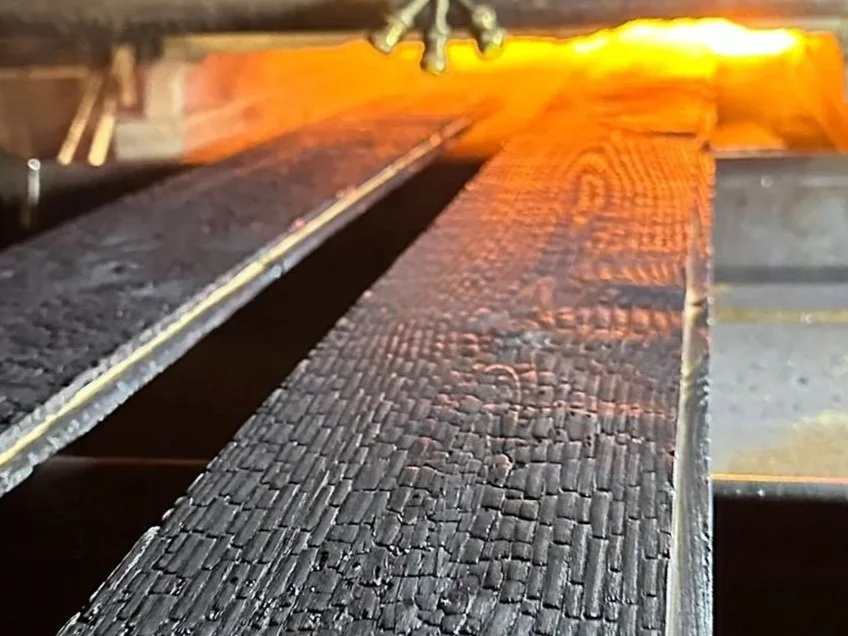 Close-up of a rough, charred wooden beam in a woodworking or fireplace setting.