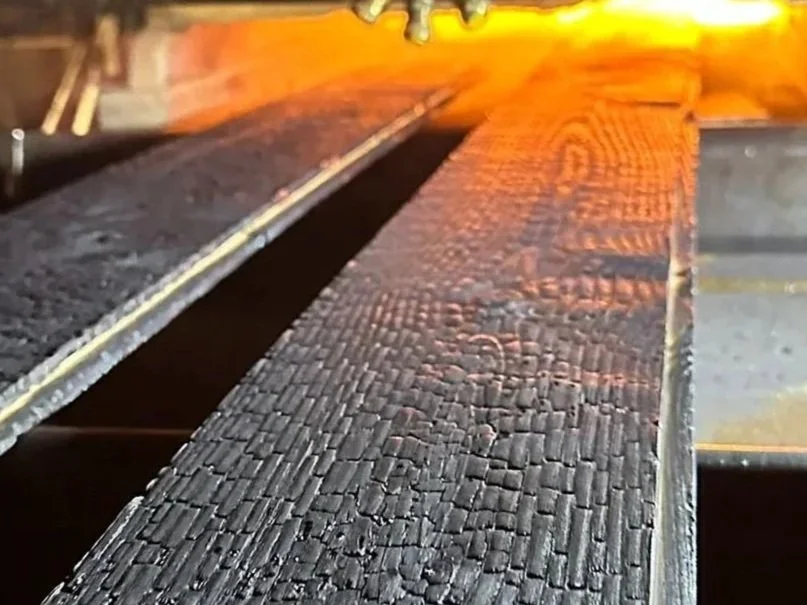 Close-up of a burning wooden plank with charred, blackened surface.