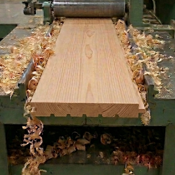 A woodworking machine shaping a large piece of wood, with wood shavings around it.