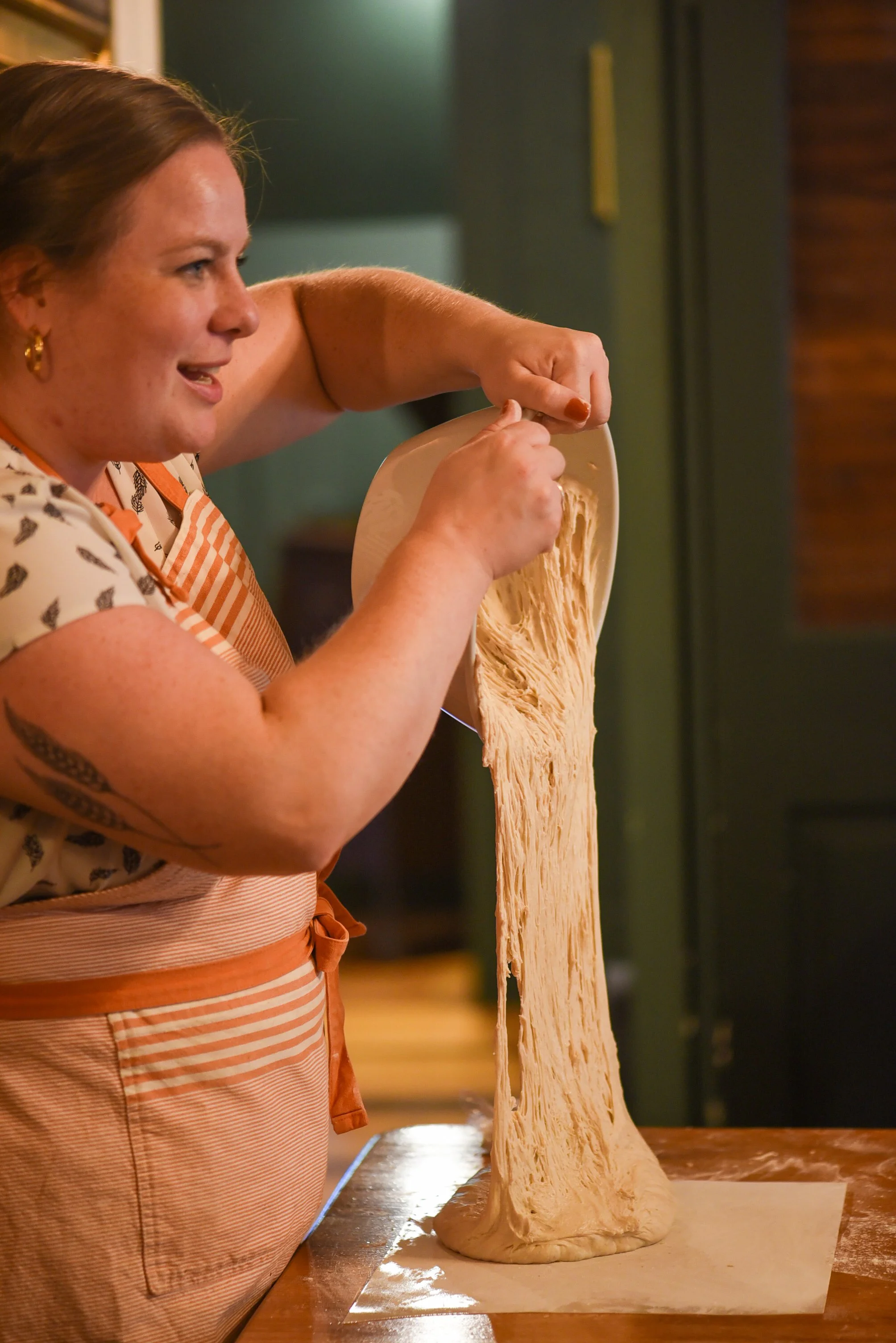 Woman stretching bread dough on a wooden counter.