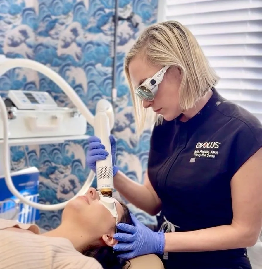 A healthcare professional performing a facial treatment with a specialized device on a woman lying down in a medical setting with a sea-themed wallpaper background.