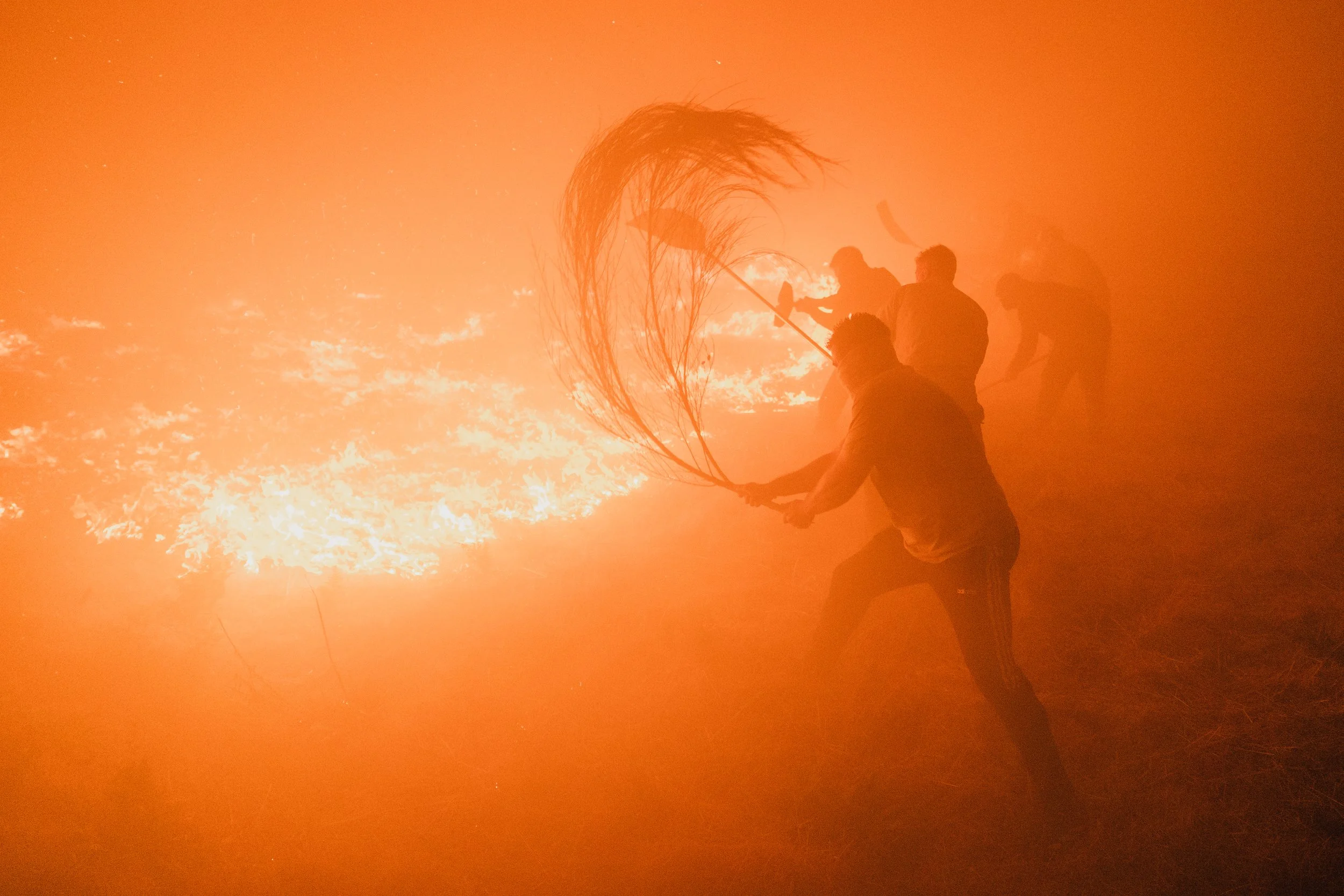 Personas intentando apagar un incendio con un escudo de fuego en un campo.