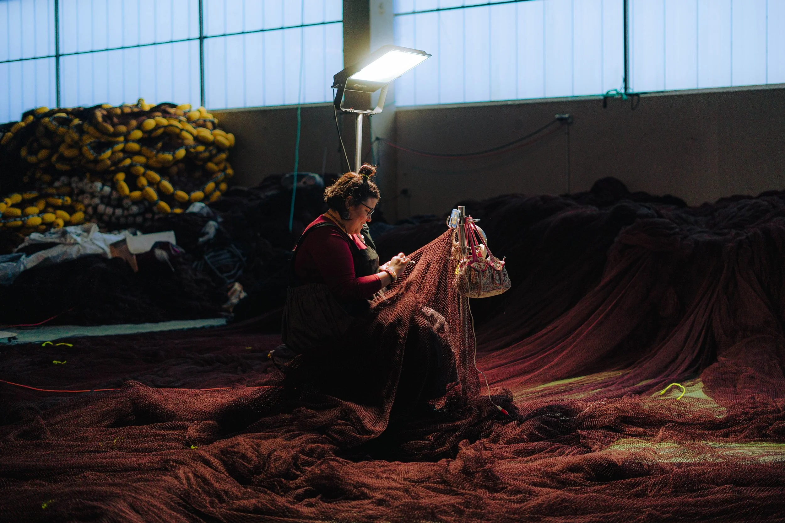 Persona trabajando en una fábrica de redes de pesca en interiores con luz artificial.