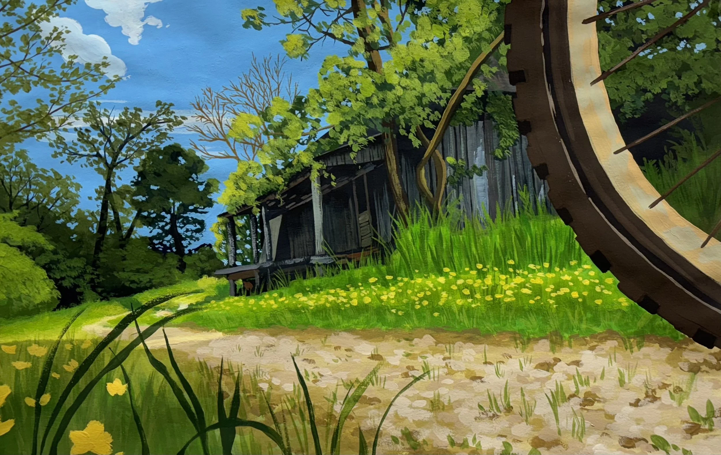 A painted mural of a rustic wooden house surrounded by trees and grass, with a blue sky in the background, and part of a large bicycle wheel in the foreground.