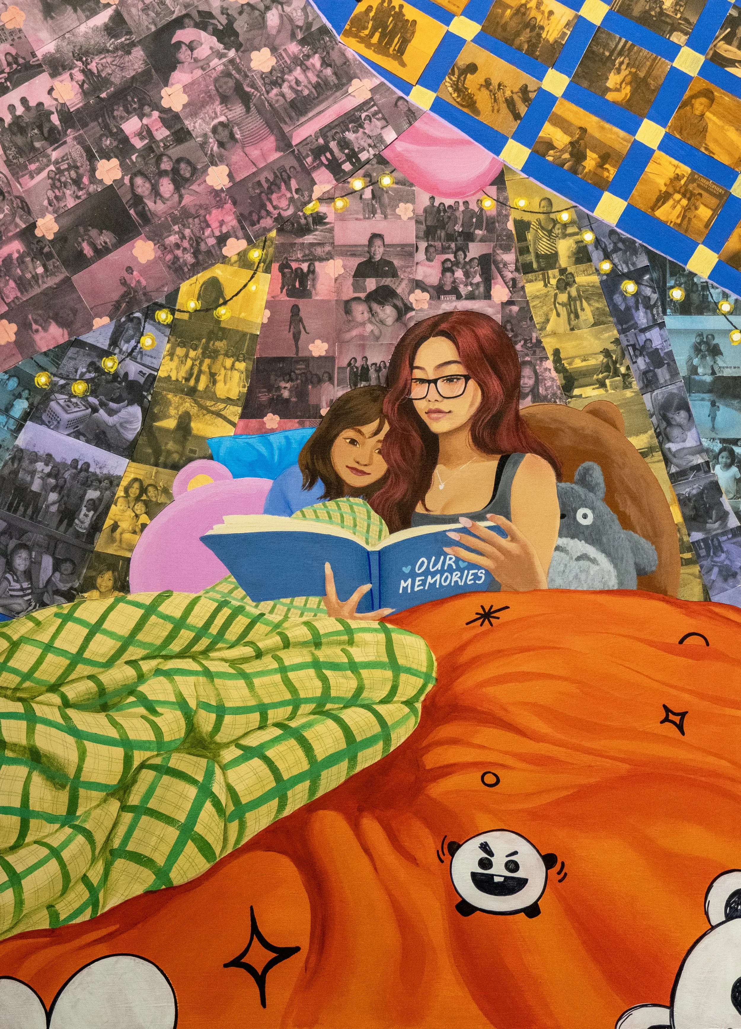 Colorful mural featuring two women, one with glasses and red hair and the other with brown hair, reading a photo album titled 'Our Memories' while lying in bed covered with a green and yellow checkered blanket. The background is decorated with photographs, fairy lights, and cartoonish characters.