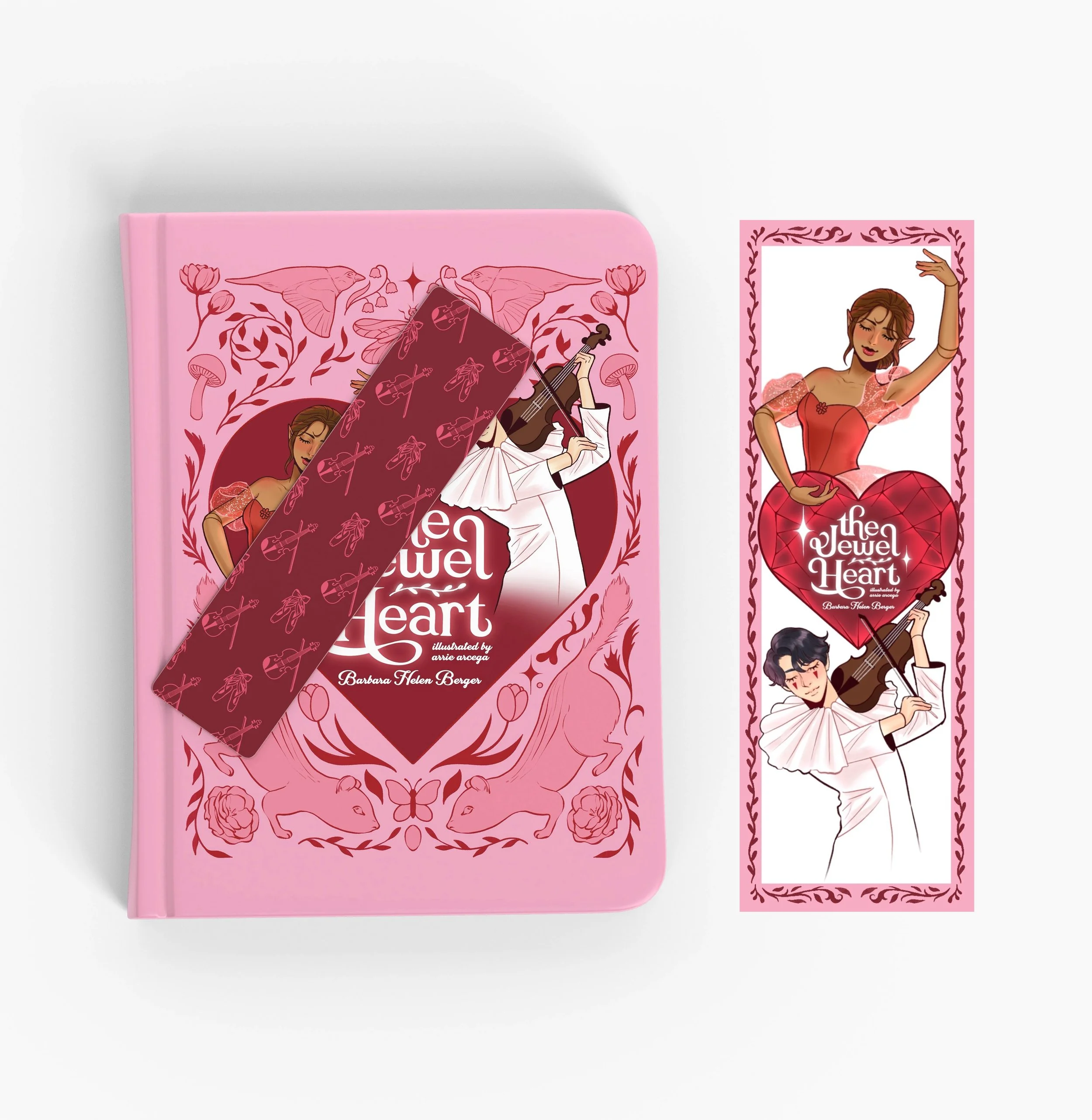 A pink hardcover book titled 'The Jewel Heart' with an illustrated cover of two characters playing violin, surrounded by floral and animal designs. Next to the book is a matching bookmark featuring the same illustrated characters and floral border.