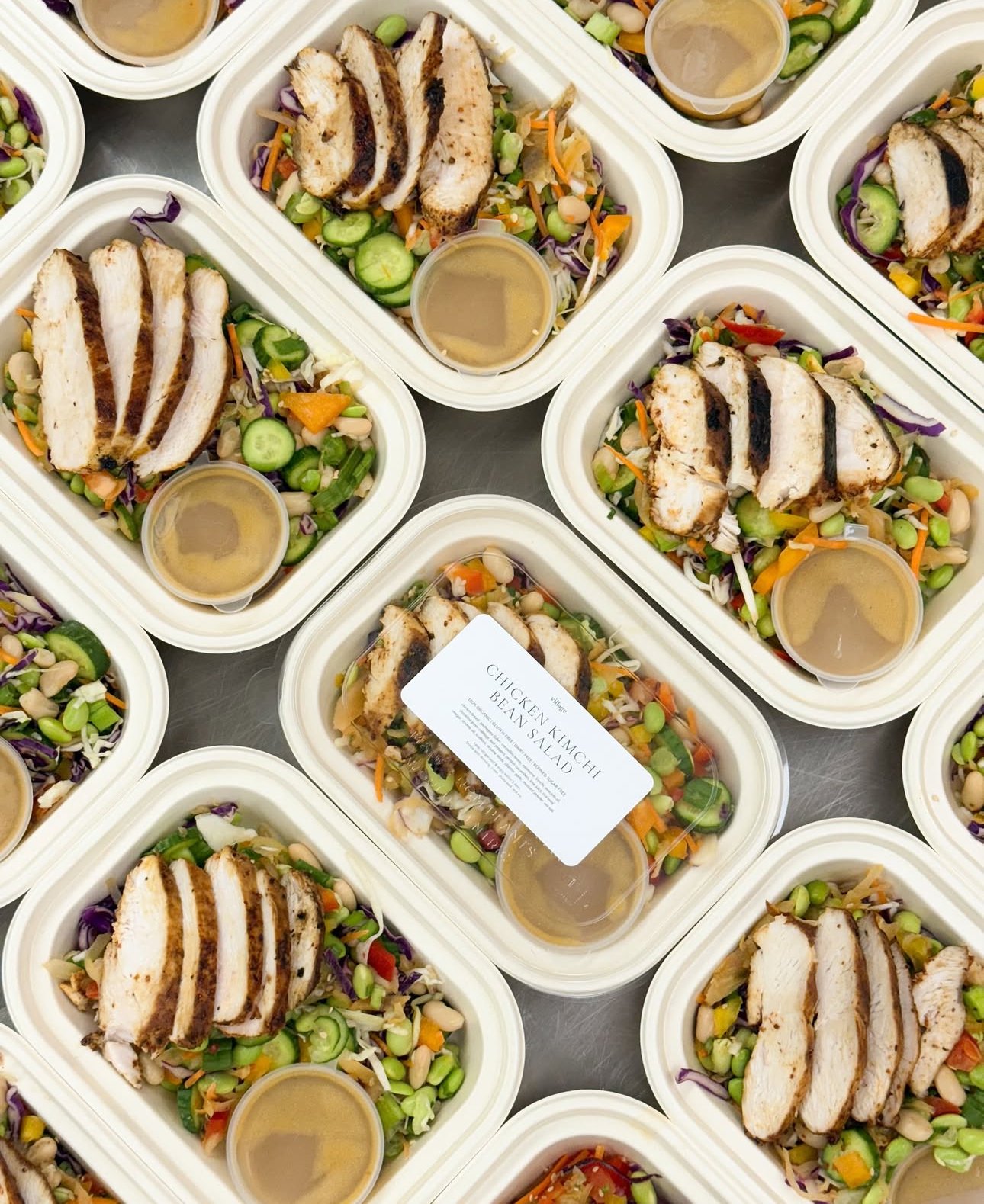 Containers of chicken kimchi bean salad with sliced grilled chicken, vegetables, and dressing.