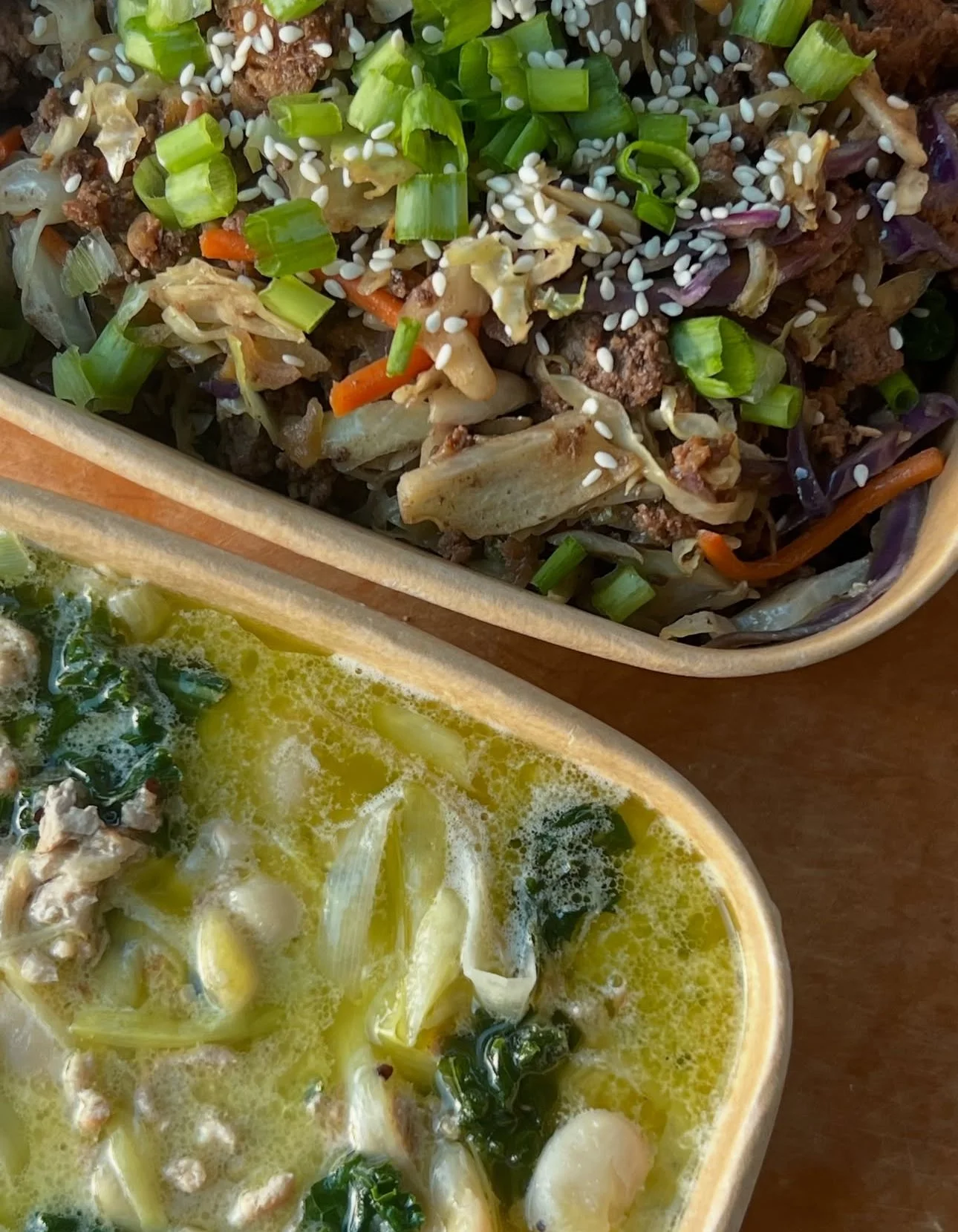 Close-up of two dishes: a beef and vegetable stir-fry topped with chopped green onions and sesame seeds, and a bowl of hot soup with leafy greens and sliced vegetables.