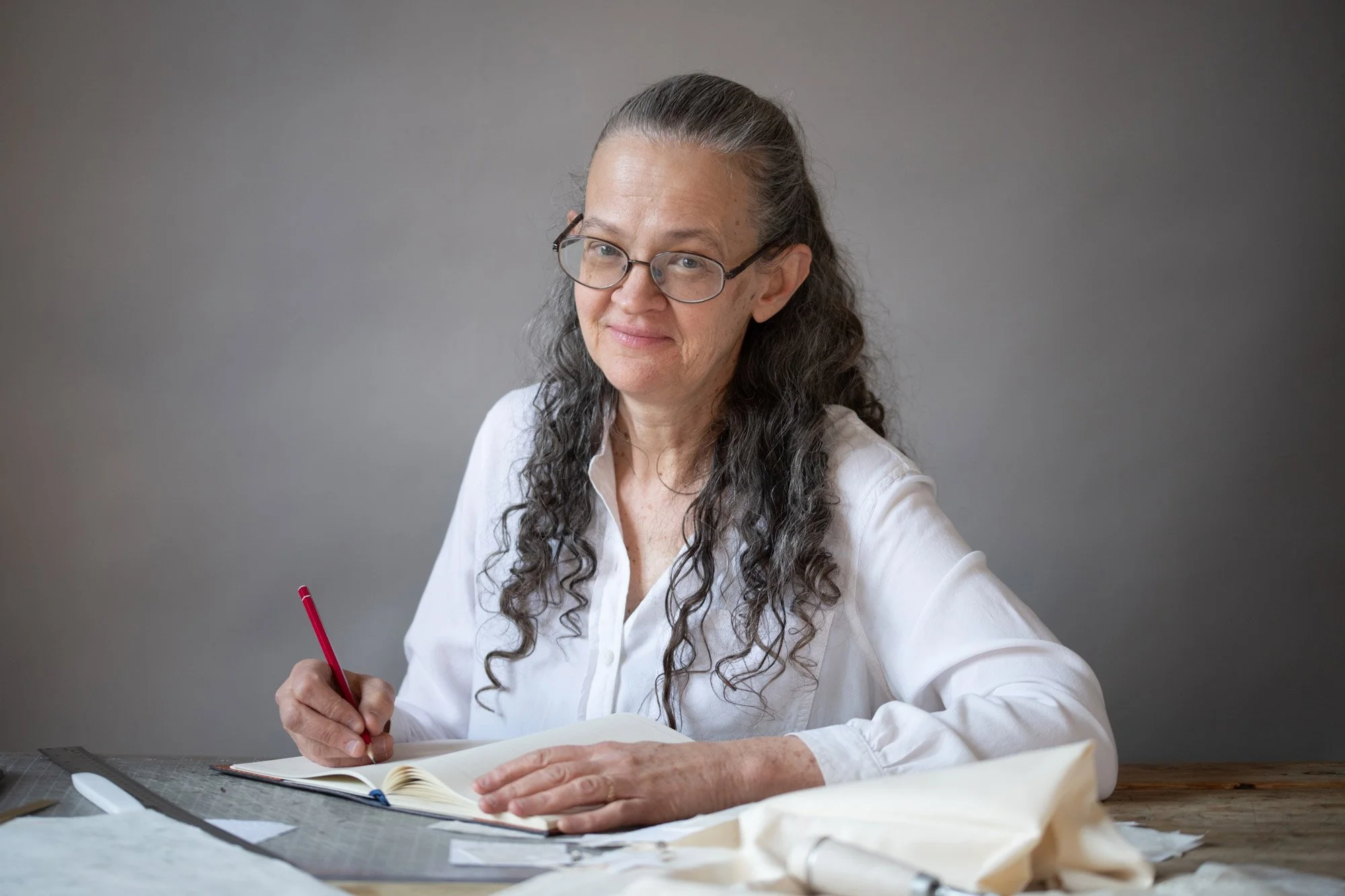Heather Doyle-Maier sitting at a table holding a red pen, smiling
