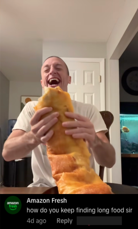 A man sitting at a table holding and eating a large slice of cheese pizza, with a humorous expression, in a home setting.