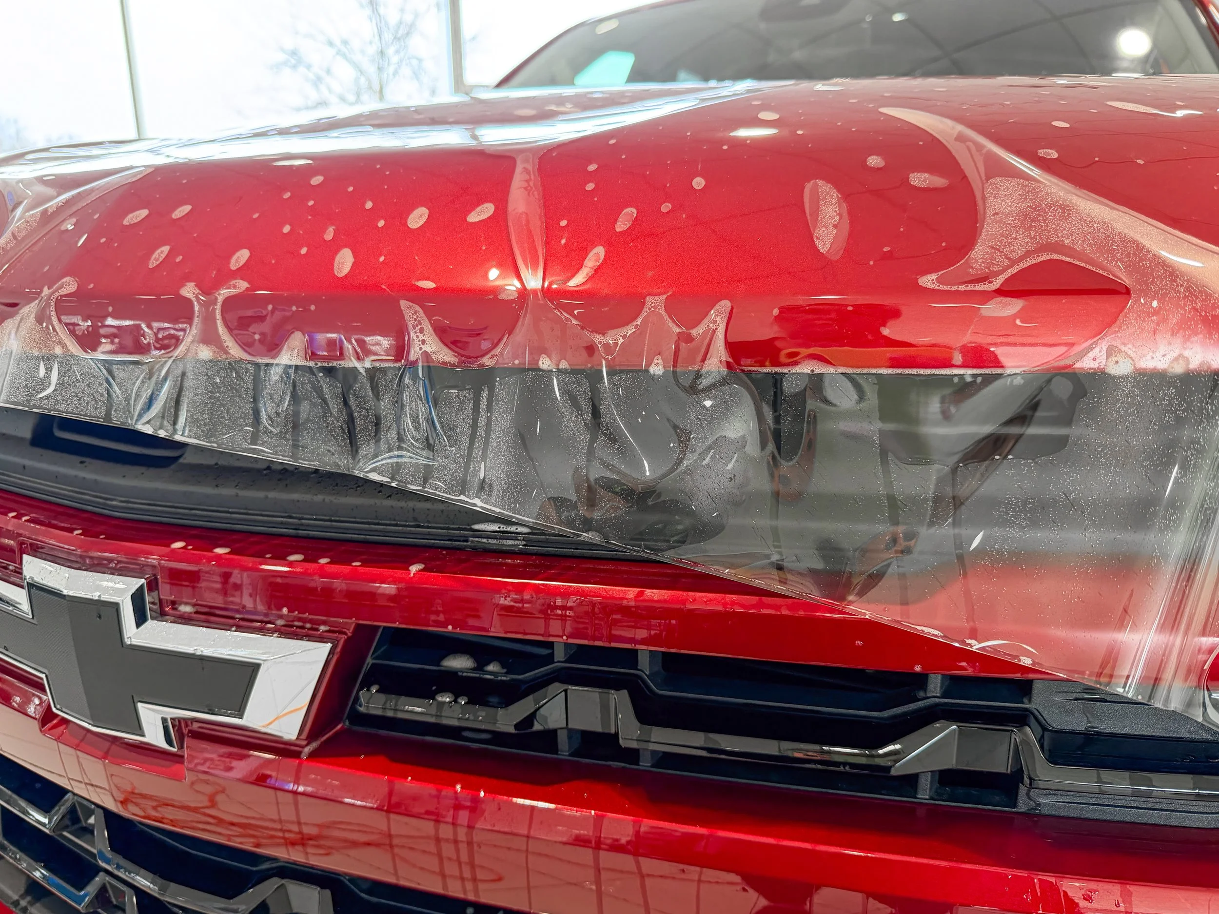 Close-up of XPEL paint protection film and slip solution on a red Chevy truck hood in Bridgeville, PA.